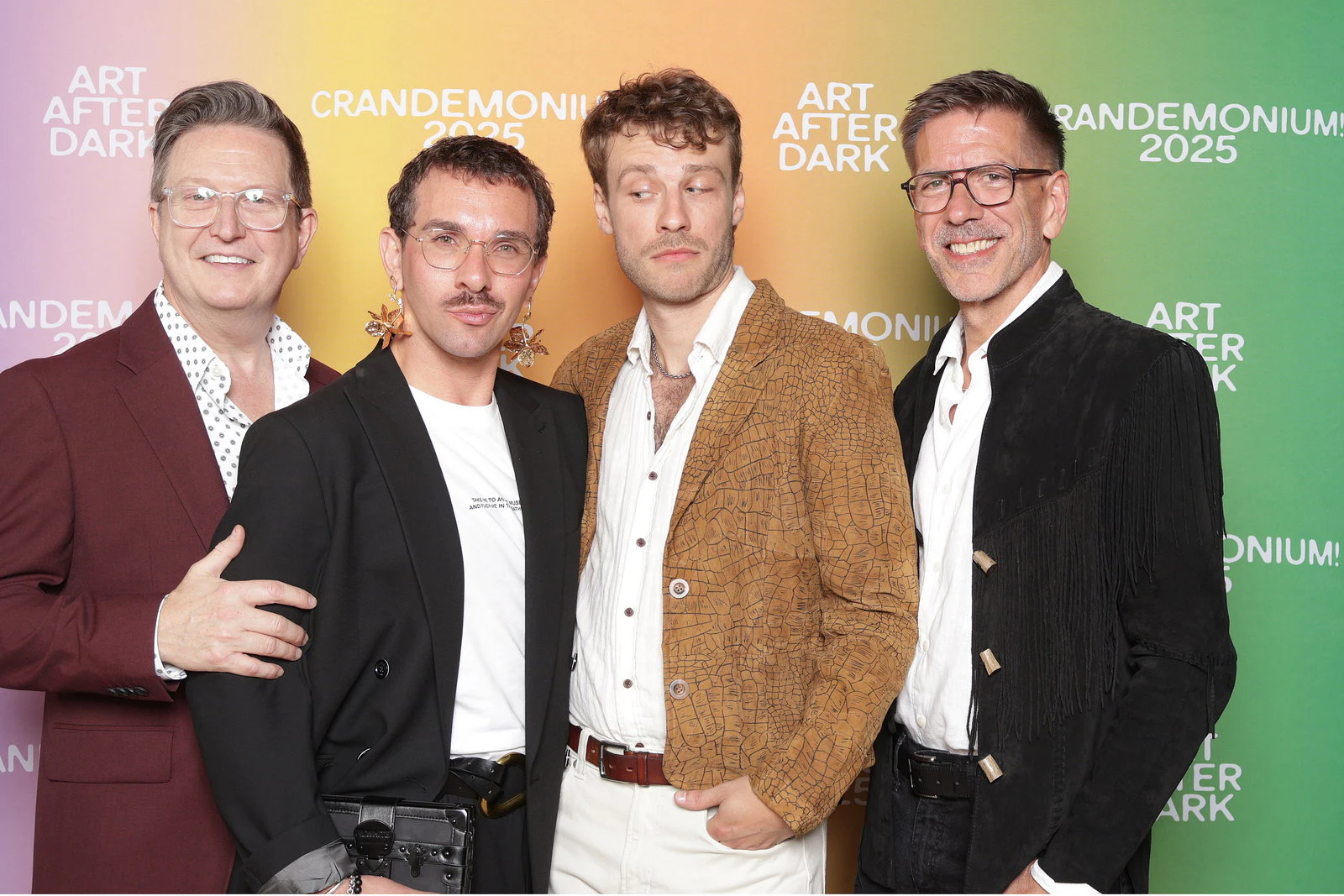 Four men in jackets standing close in front of the pastel Crandemonium background at Crandemonium 2025