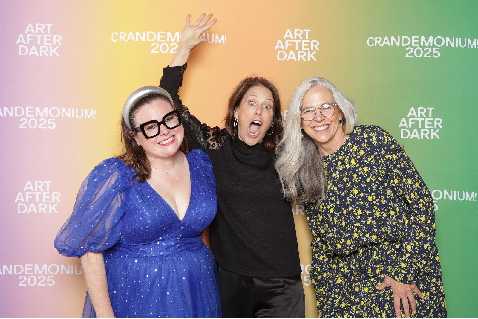 Three women, one in a blue sparkly dress and big black glasses, one waving an arm behind her at Crandemonium 2025