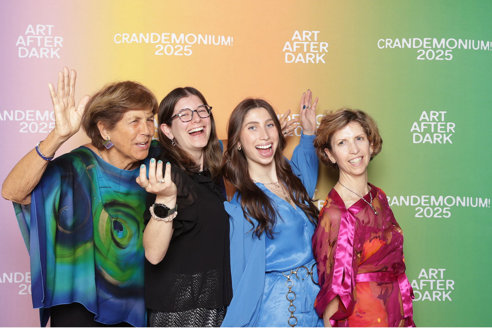 Four women in bright dresses waving in front of the pastel background at Crandemonium 2025