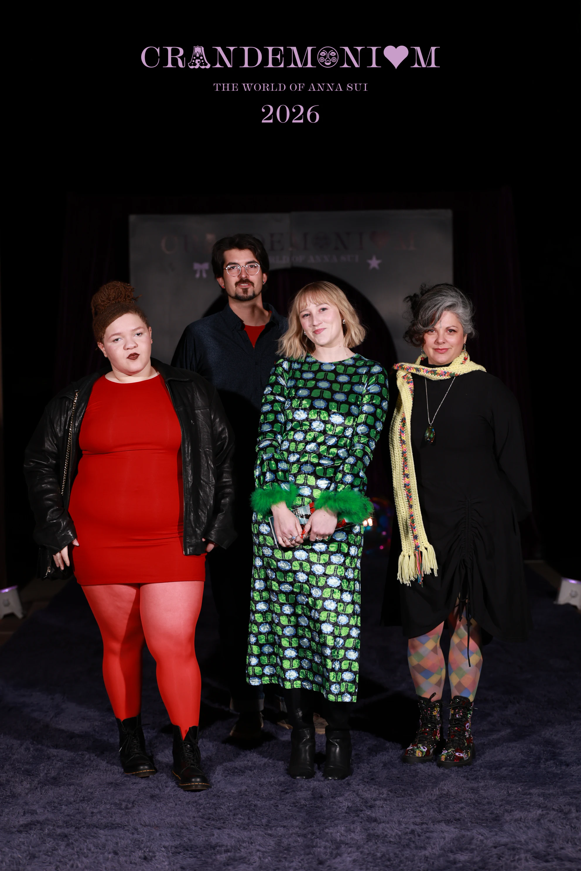 Four guests in front of the arch at night, one in a red dress and one in a green sequin dress with feathered cuffs at Crandemonium 2026