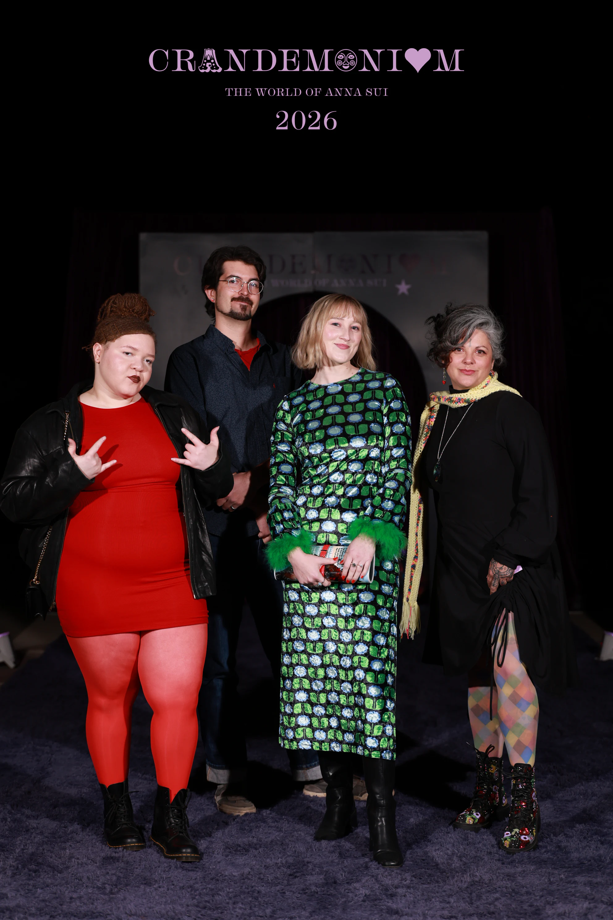 The woman in red throwing rock-on hands while the others smile at Crandemonium 2026
