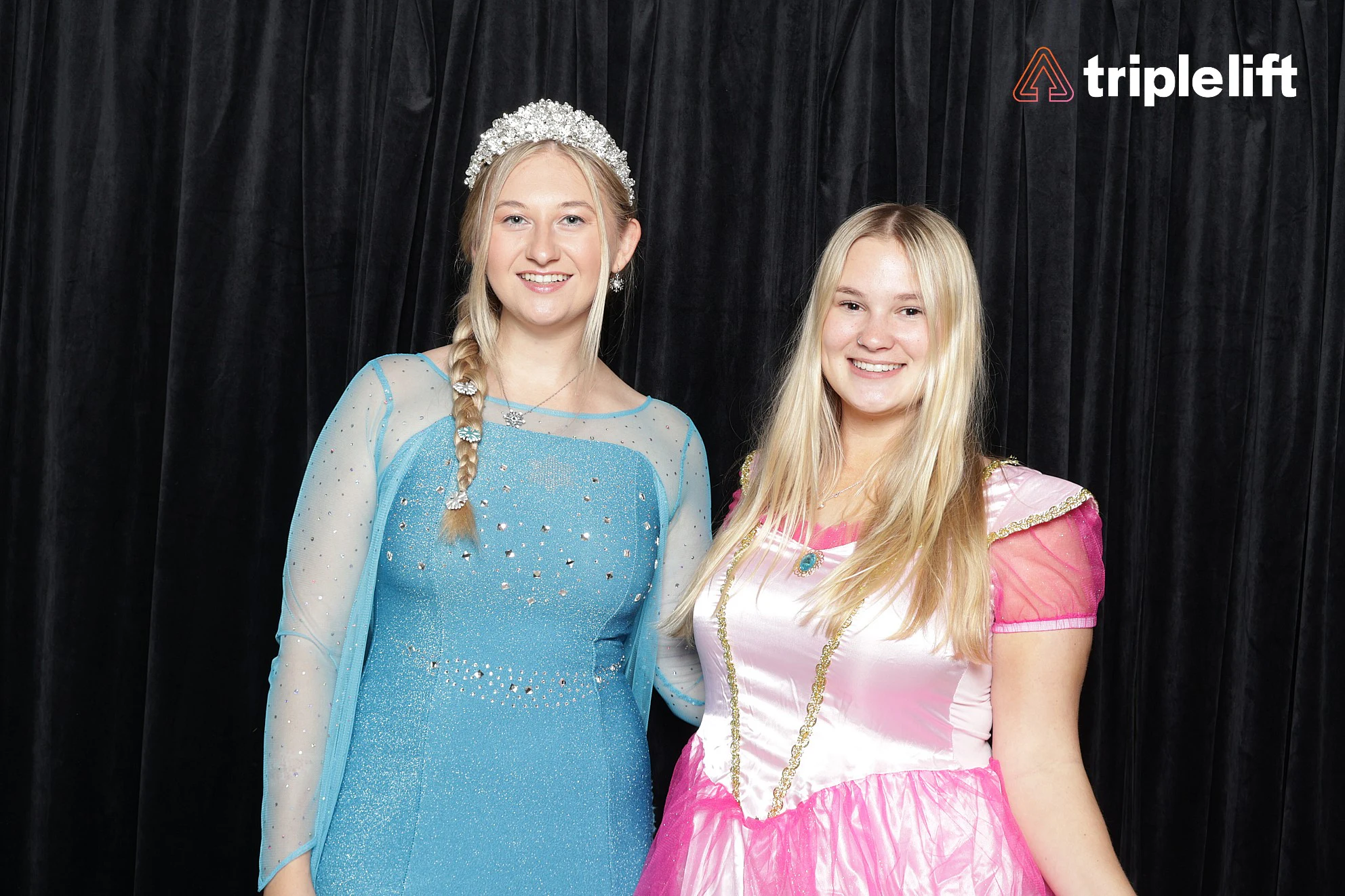 Two women in blue and pink princess gowns, one wearing a tiara, side by side at TripleLift Halloween Party