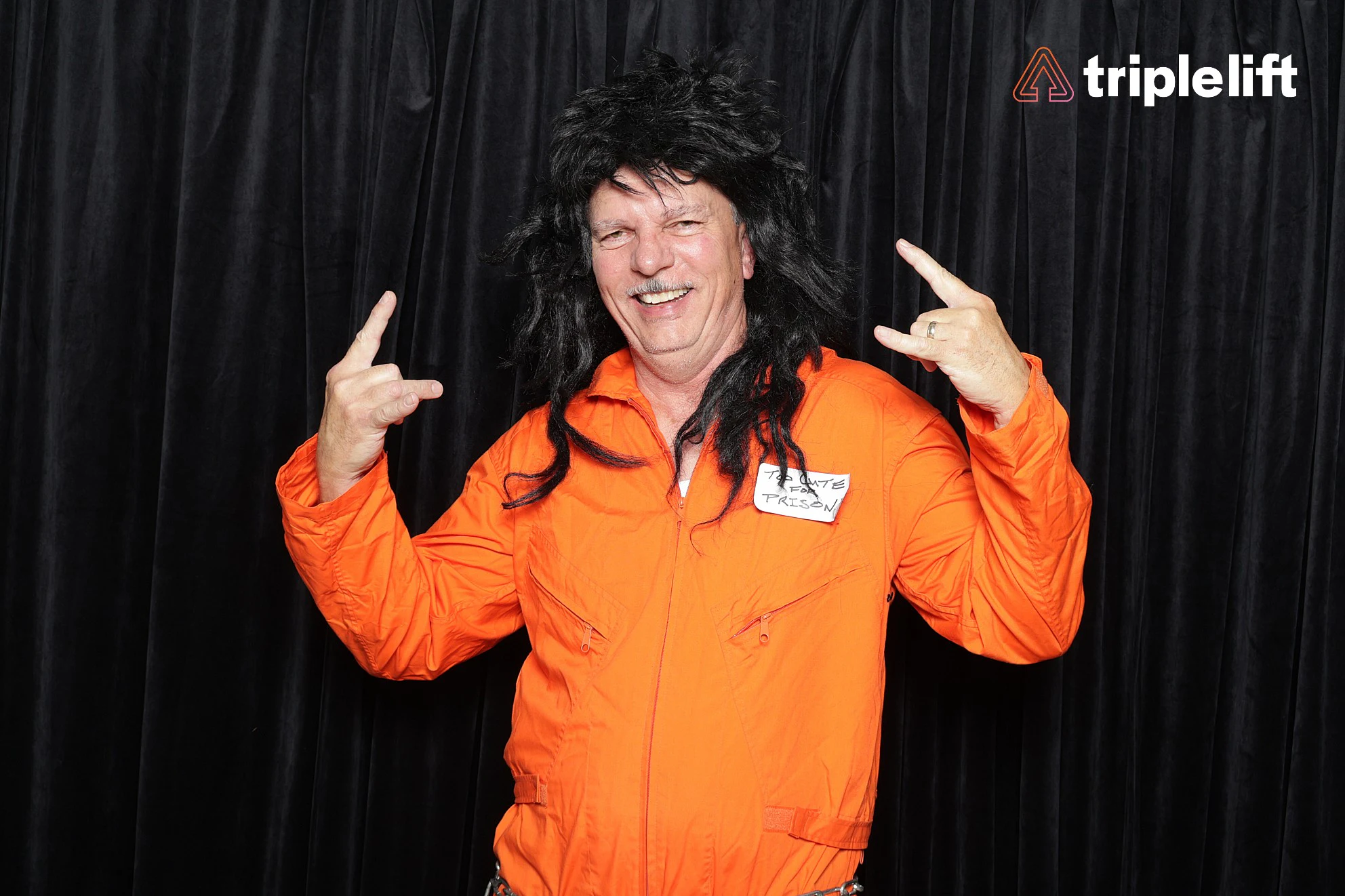 A man in an orange jumpsuit and a shaggy black wig throwing rock hand signs at TripleLift Halloween Party
