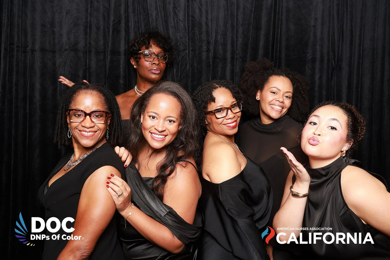 Seven women in black dresses in front of the black velvet drape at DNPs of Color
