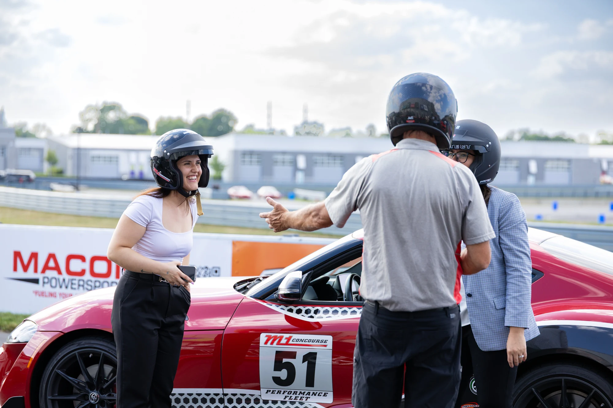Two guests with the instructor at the red track car at Dykema Automotive Legal Summit 2026