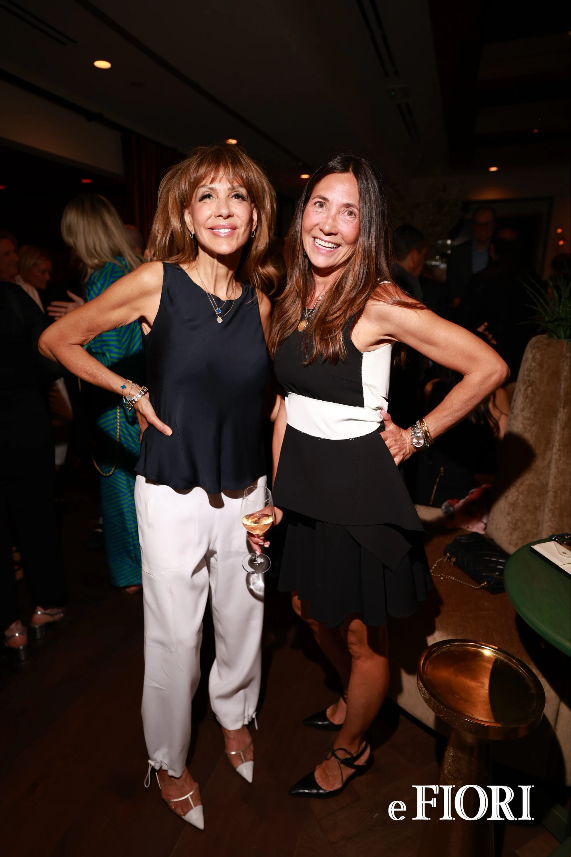 Two women posing with hands on hips, one holding a glass of wine at e Fiori Birmingham Opening Party