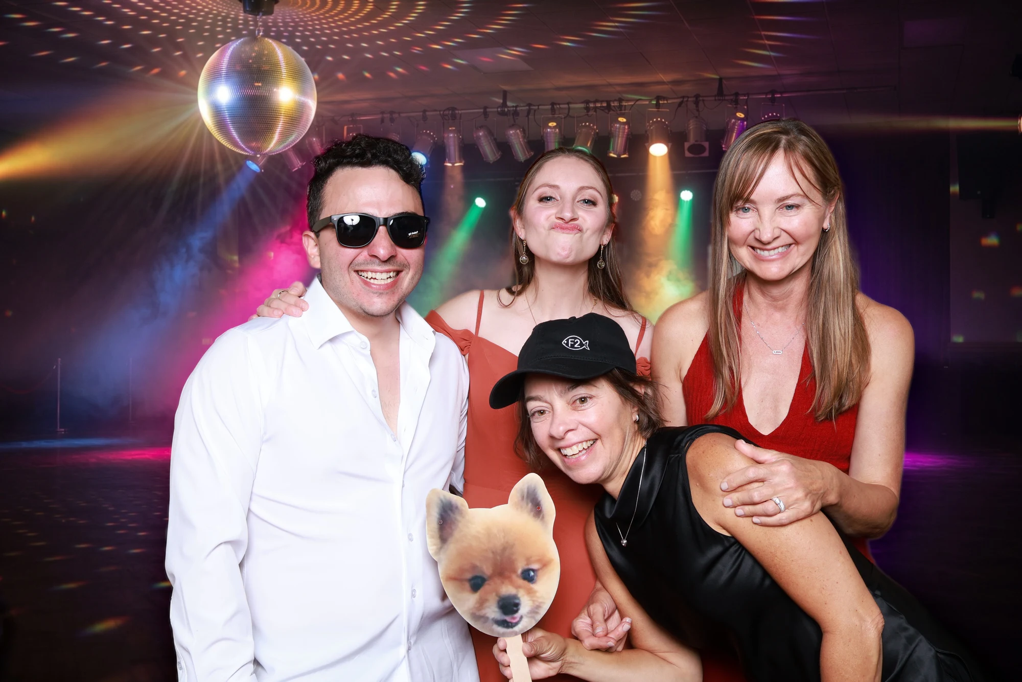 Four guests on a disco backdrop with a mirror ball, one holding a dog-face prop at Eliana + Brad