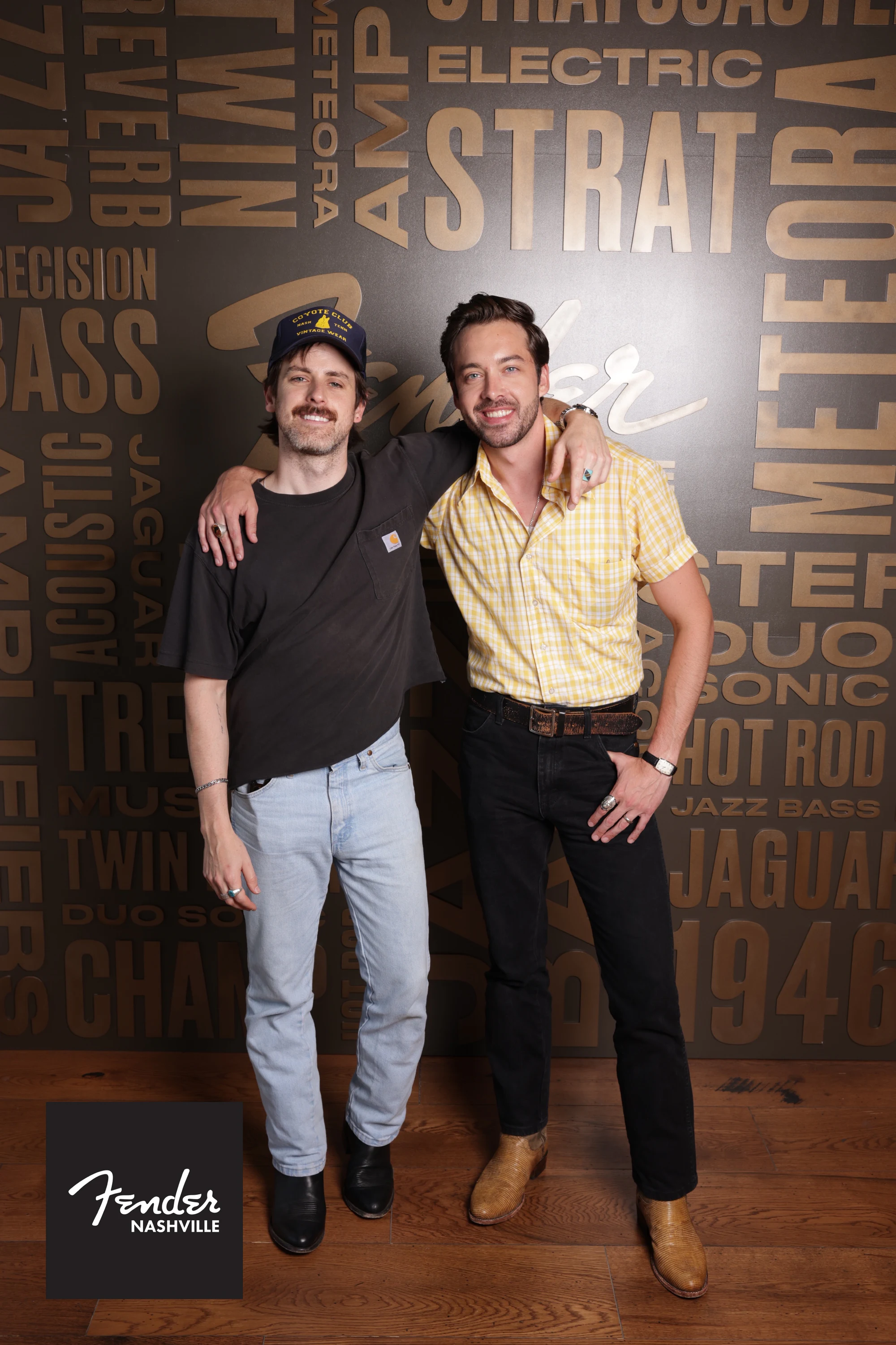 Two guests with their arms around each other against the Fender word-cloud backdrop at the Fender Nashville grand opening