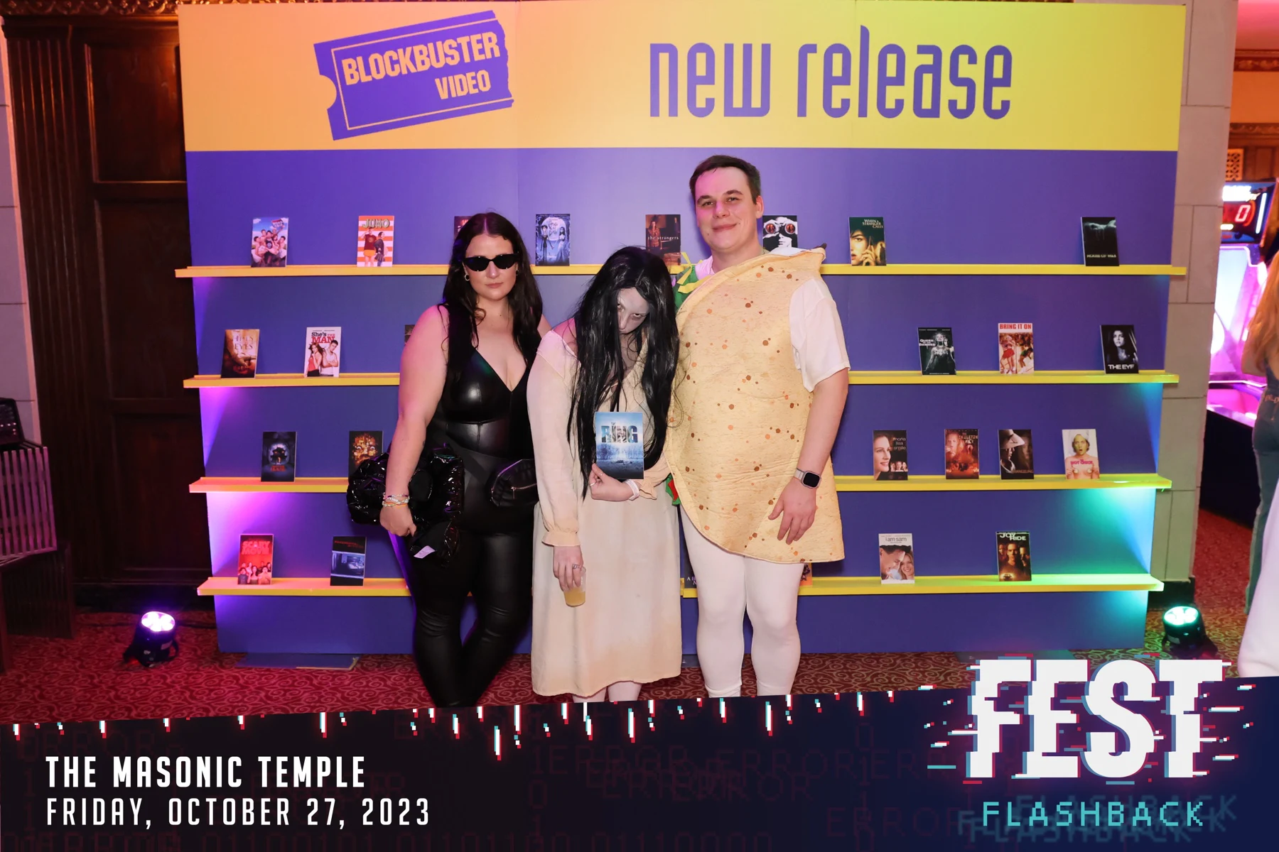 Three guests at the Blockbuster wall, one dressed as a taco, one with her hair over her face at FEST Halloween Party at the Masonic Temple