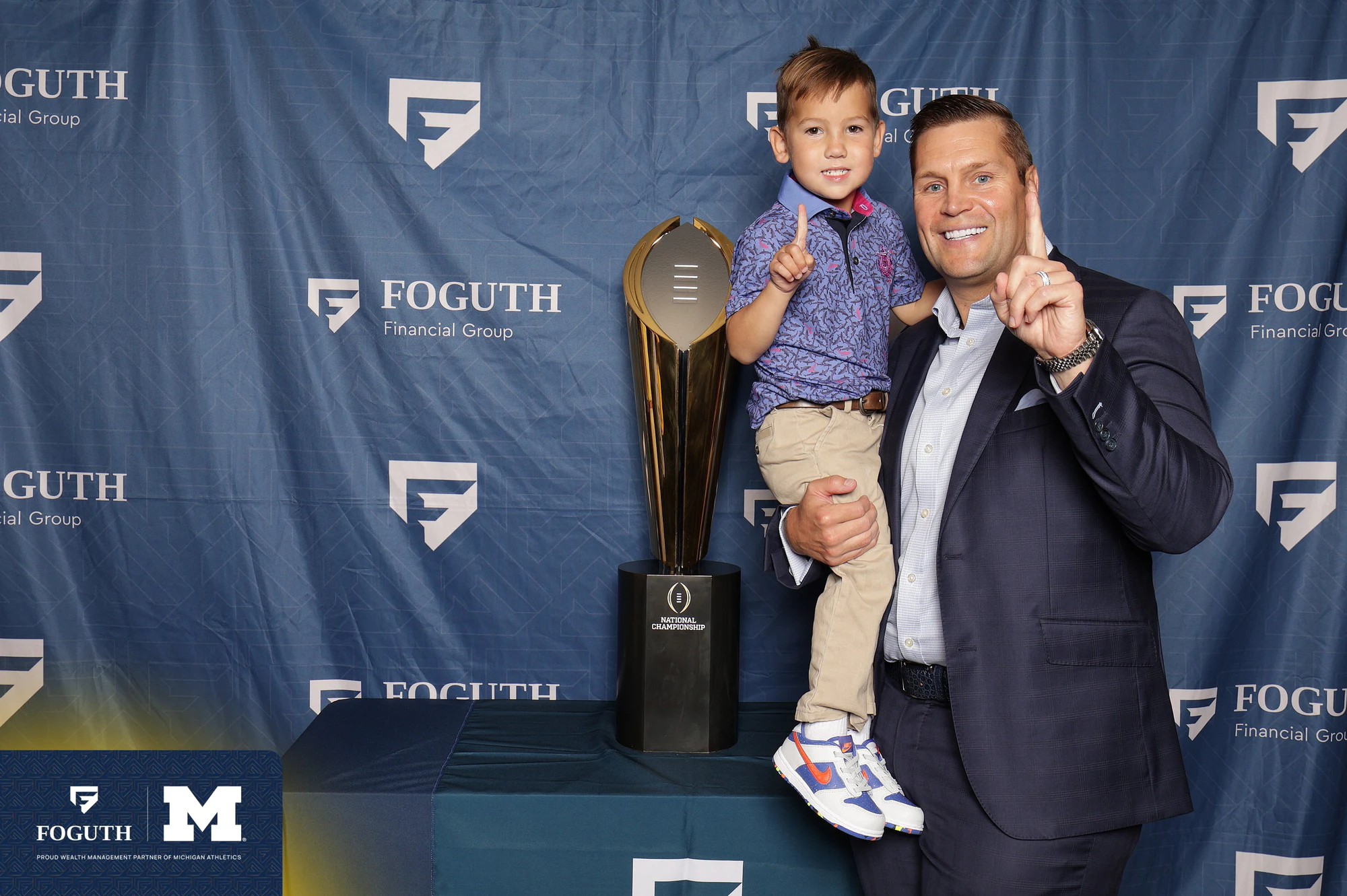 Dad holding his son next to the trophy at Foguth Financial at The Big House