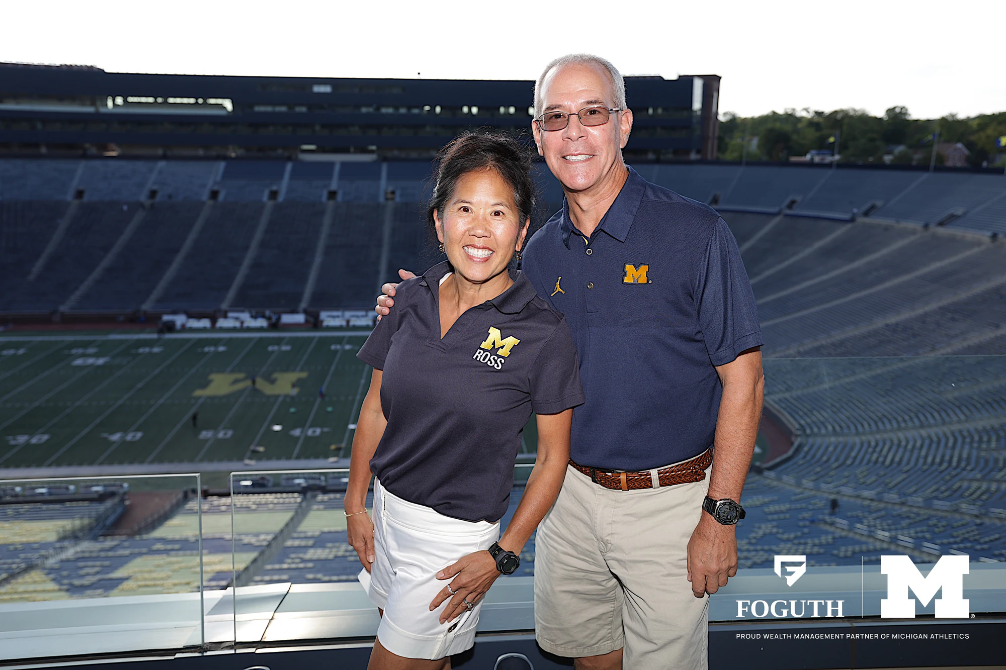Two guests in Michigan polos in a suite above the field at Foguth Financial at The Big House