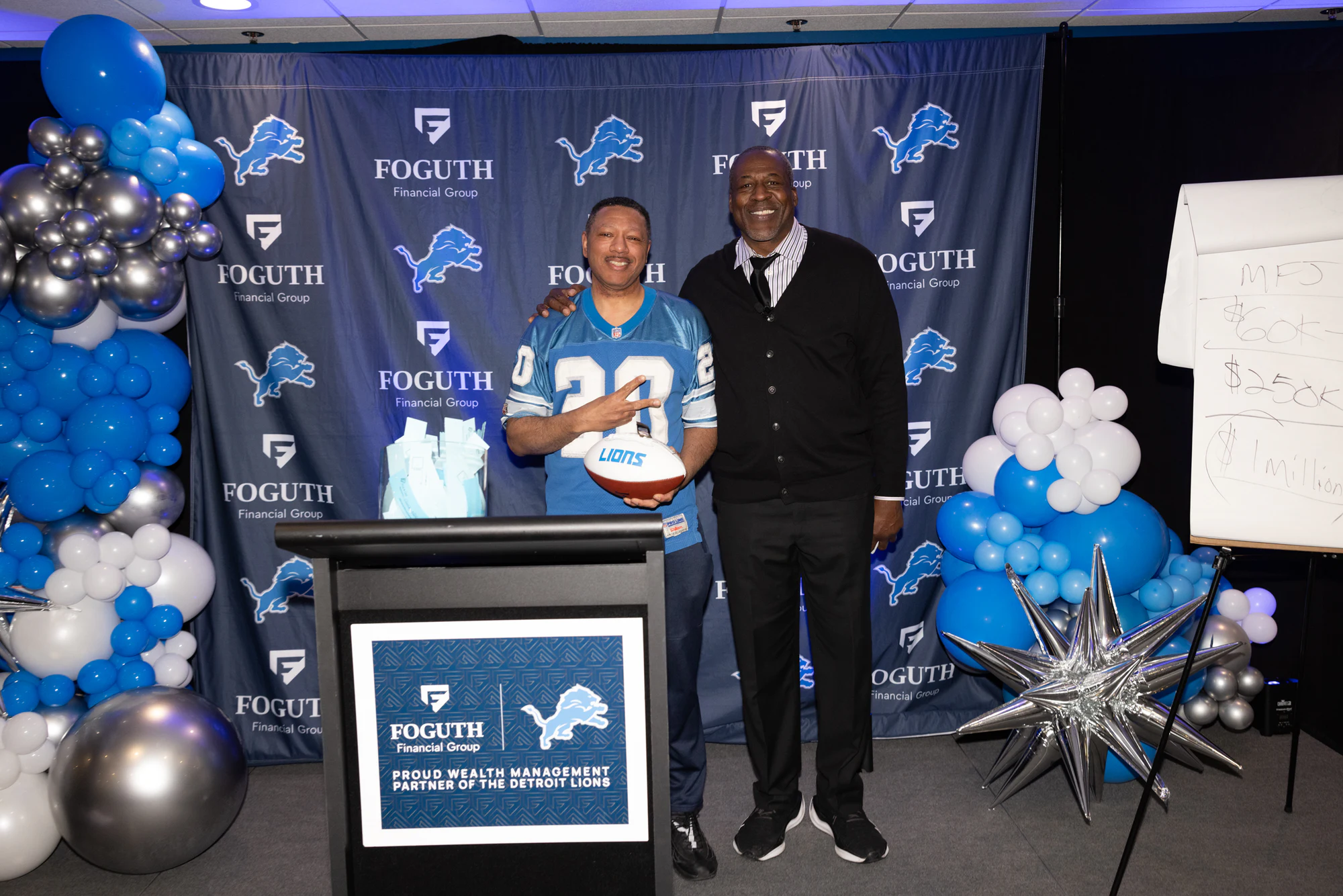 Winner holding a framed jersey, big smile, balloons behind at Foguth Financial at Ford Field