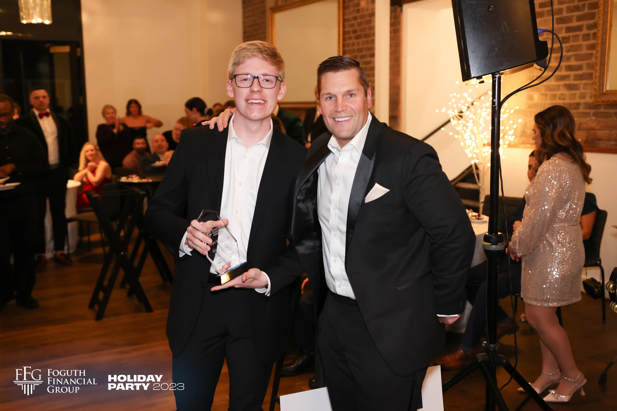 A guest holding a glass award with a man in a tuxedo at Foguth Financial Holiday Party at the Detroit Foundation Hotel