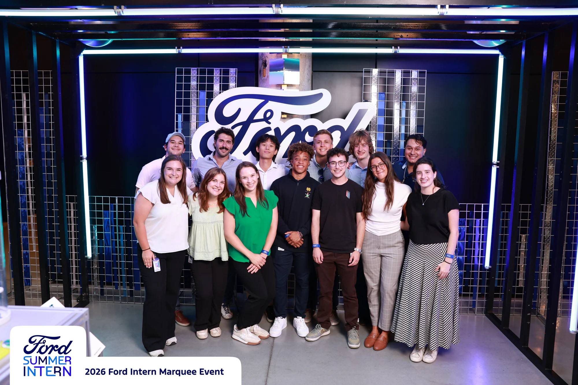 Twelve interns in two rows inside the blue LED cage at the Ford Intern Marquee Event