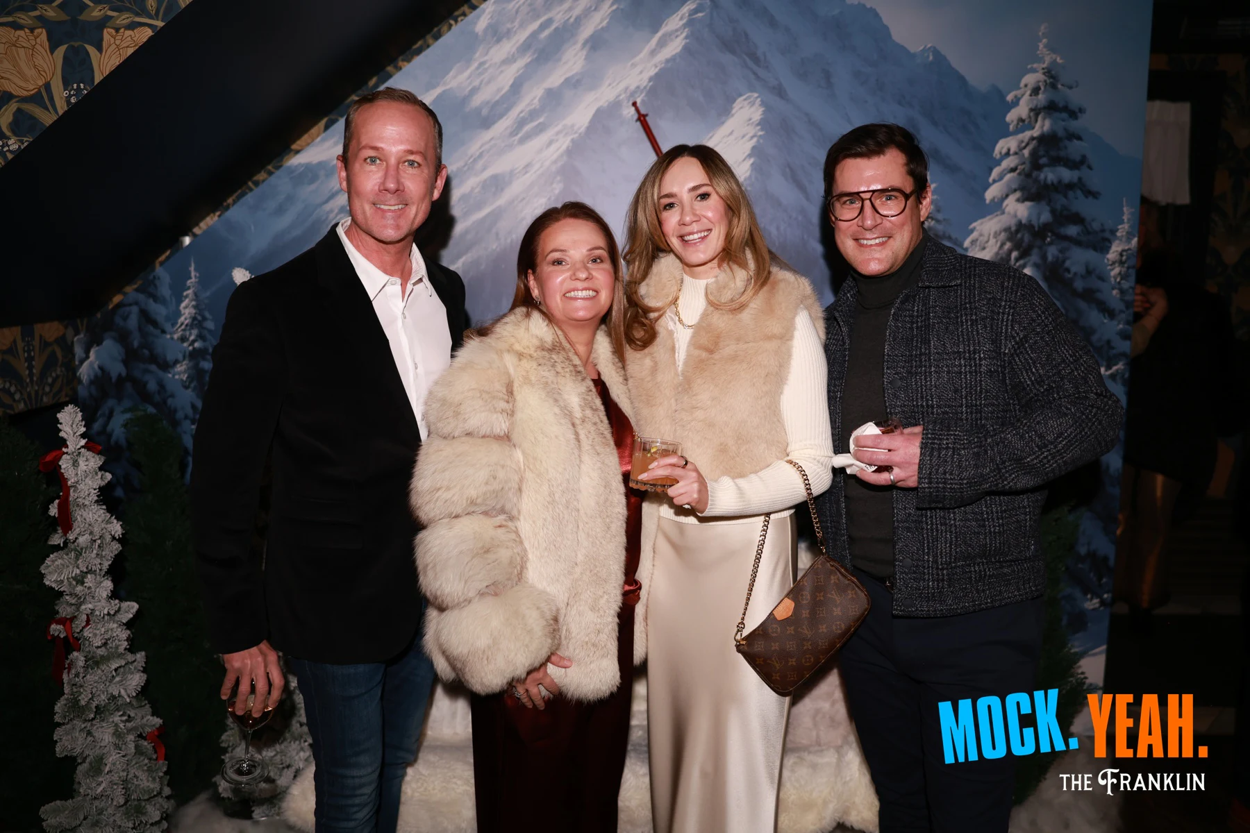 Four guests in front of the mountain backdrop, two of them in cream fur coats at the holiday party at The Franklin