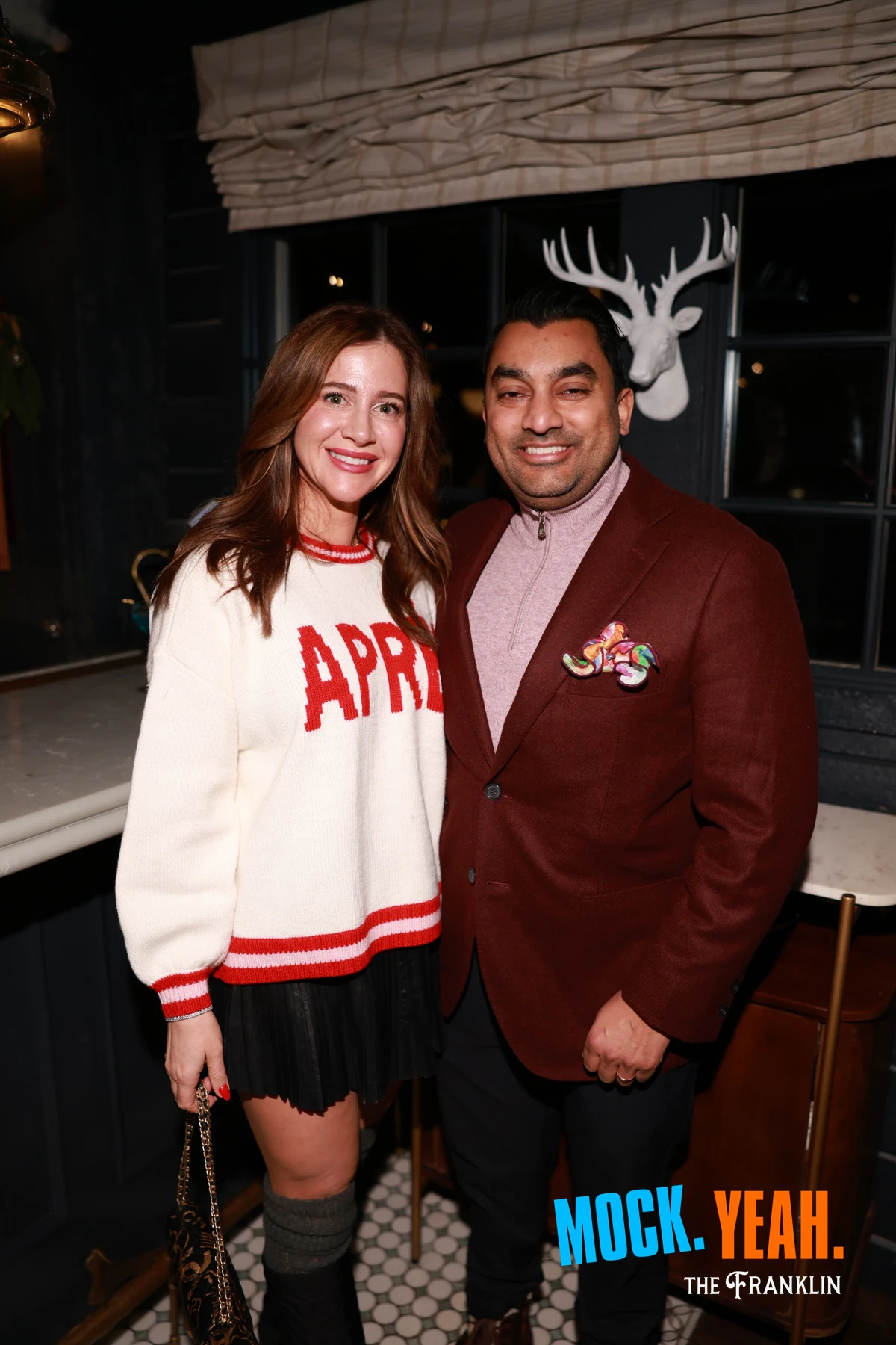 A couple by the bar, the white stag head on the wall behind them at the holiday party at The Franklin