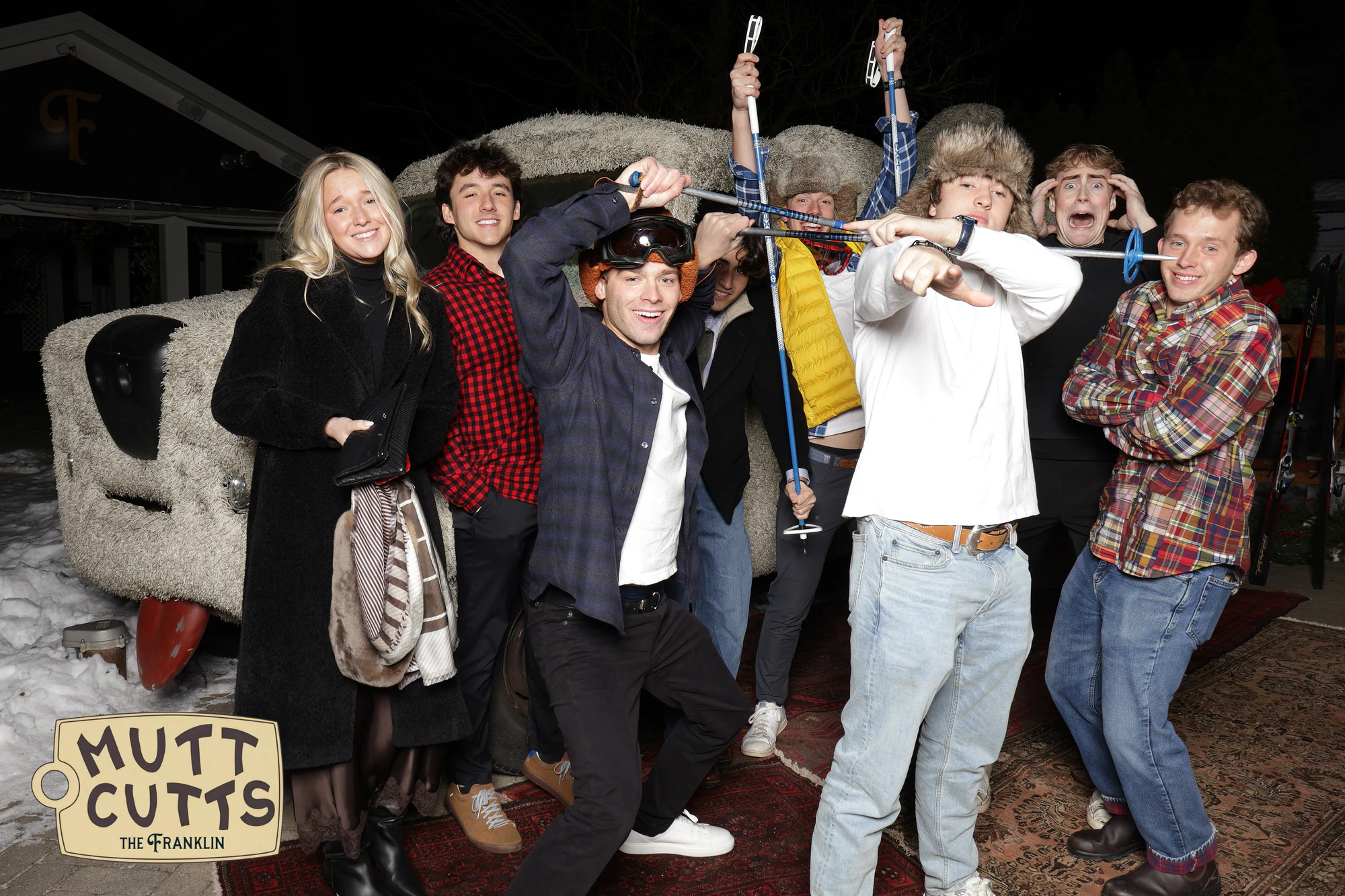 A big group in front of the shaggy Mutt Cutts van outside, ski poles held up over their heads at the holiday party at The Franklin