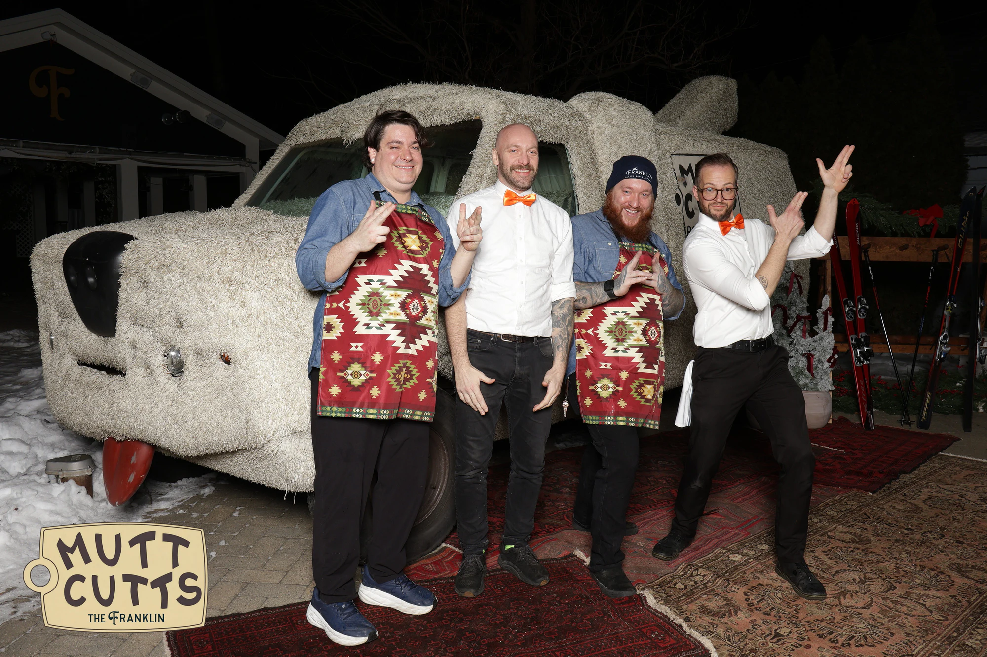 Four of the staff in orange bow ties and patterned aprons posing in front of the Mutt Cutts van at the holiday party at The Franklin