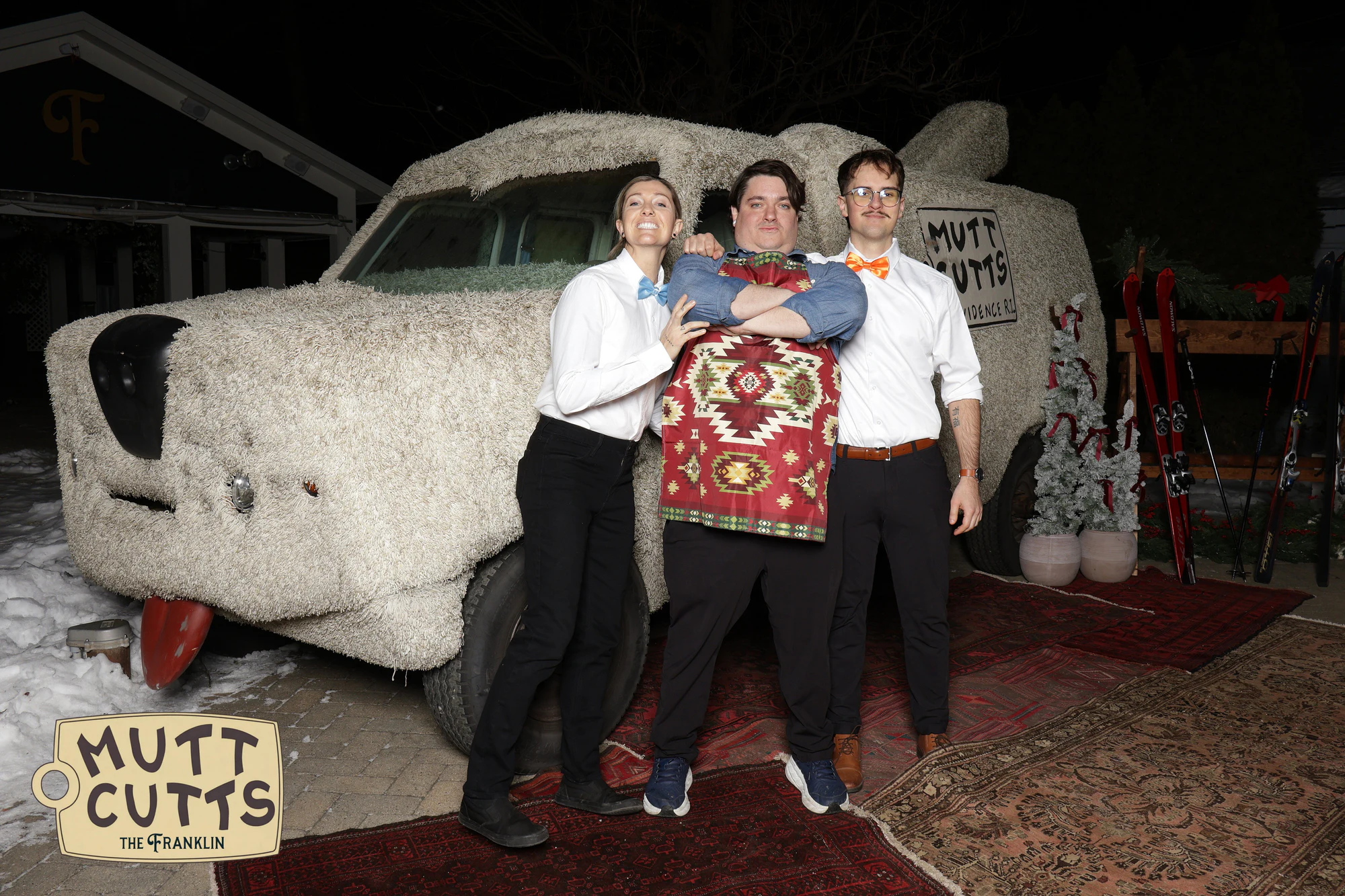 Three of the staff in bow ties, one in a patterned apron, in front of the Mutt Cutts van at the holiday party at The Franklin