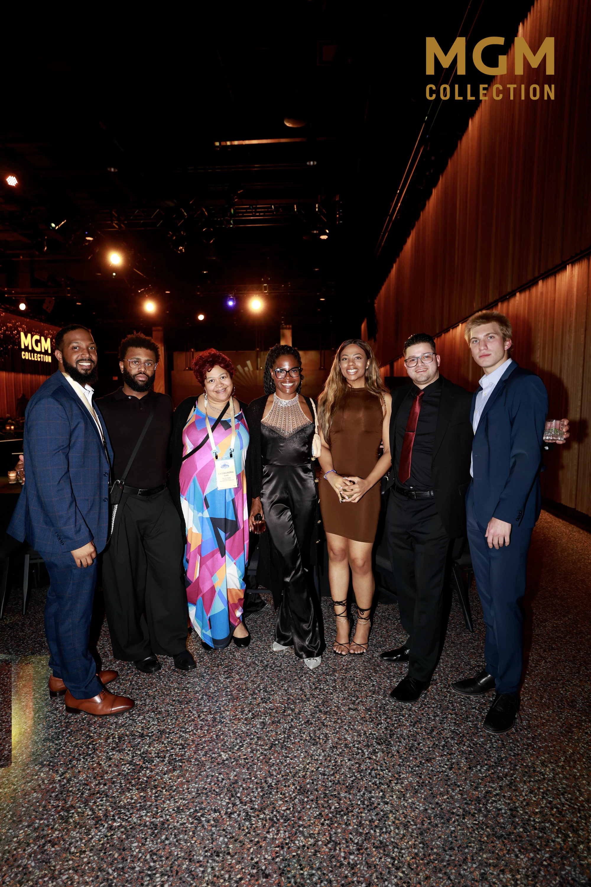 Eight friends spread across the frame under the copper wall at Fuel Our Future Gala