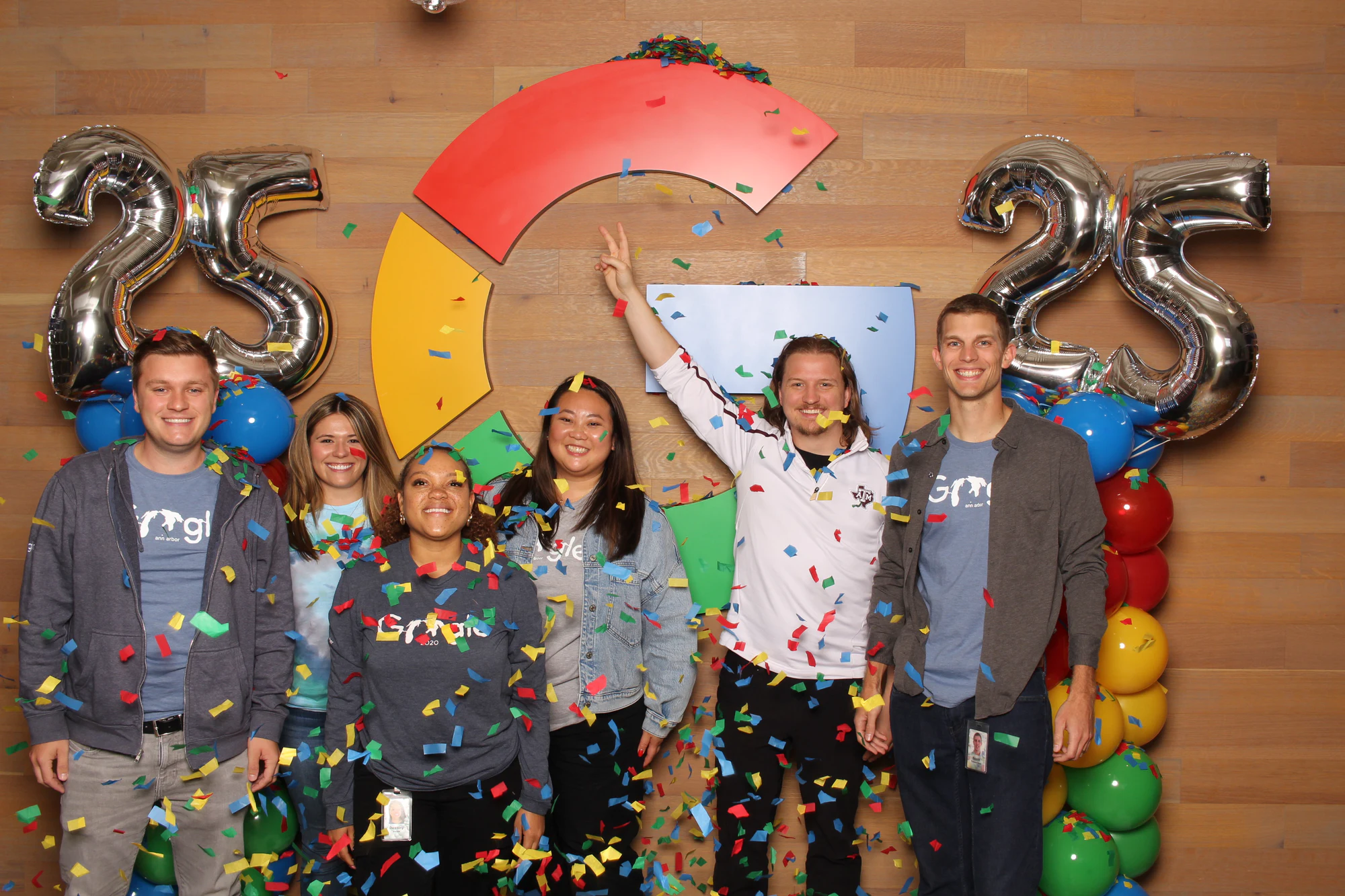 The nine with arms raised, a man in white at the back reaching up at Google’s 25th Birthday