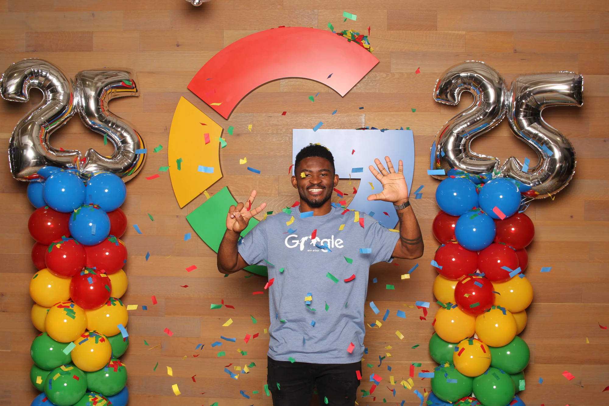 A man in a Google shirt smiling and waving in front of the Google logo at Google’s 25th Birthday