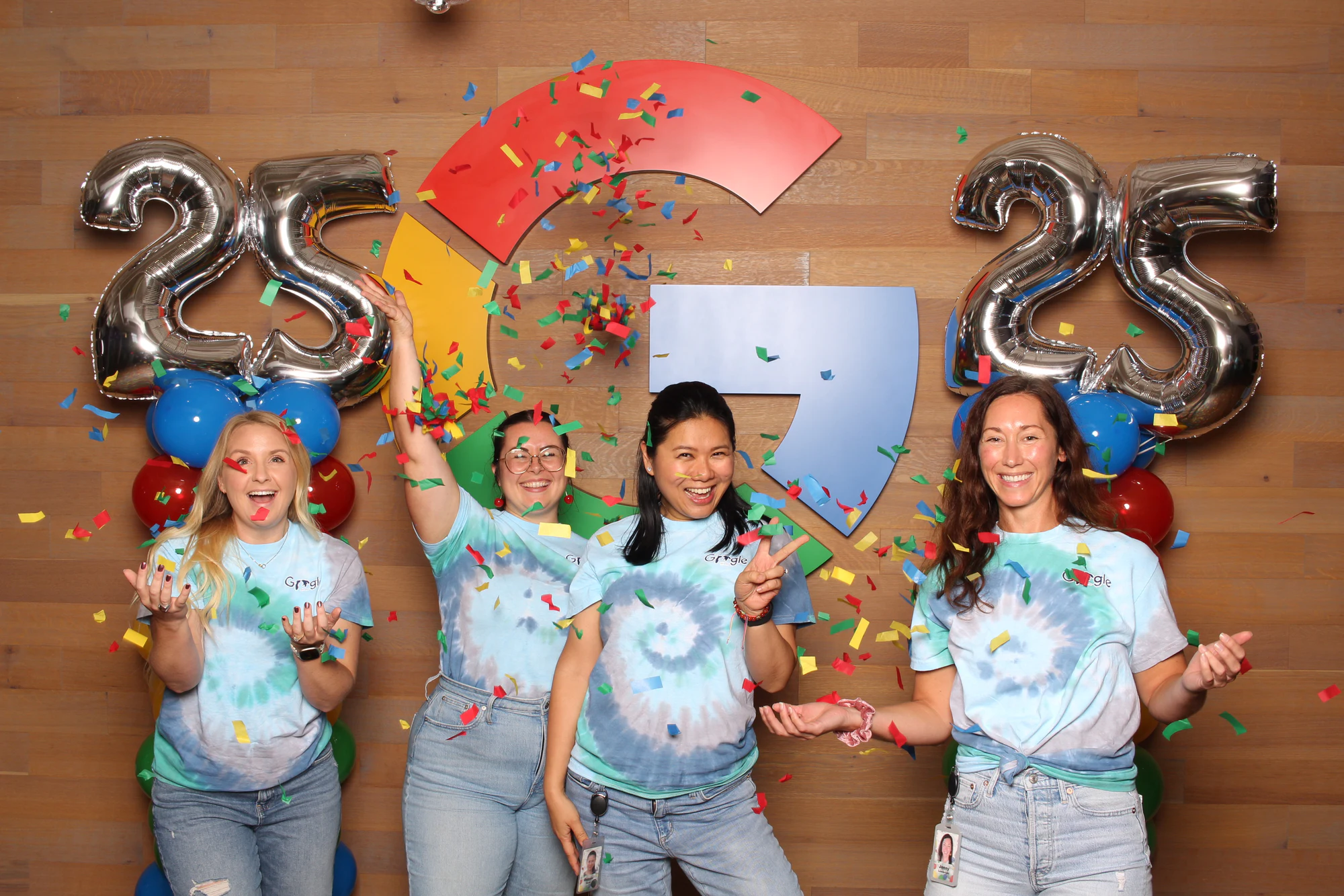 Four women in tie-dye shirts tossing confetti at Google’s 25th Birthday