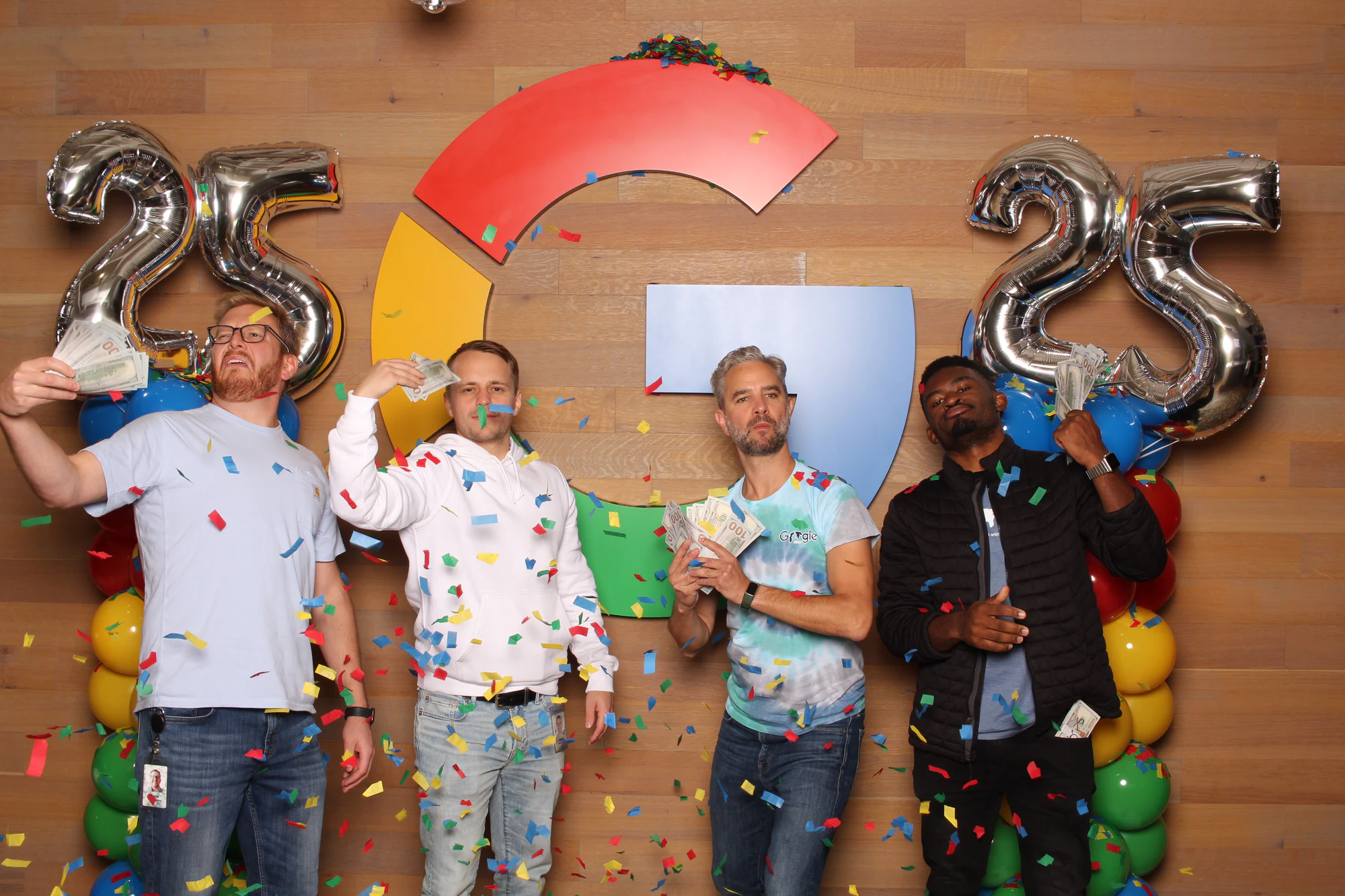 Four men throwing paper into the air in front of the silver 25 balloons at Google’s 25th Birthday