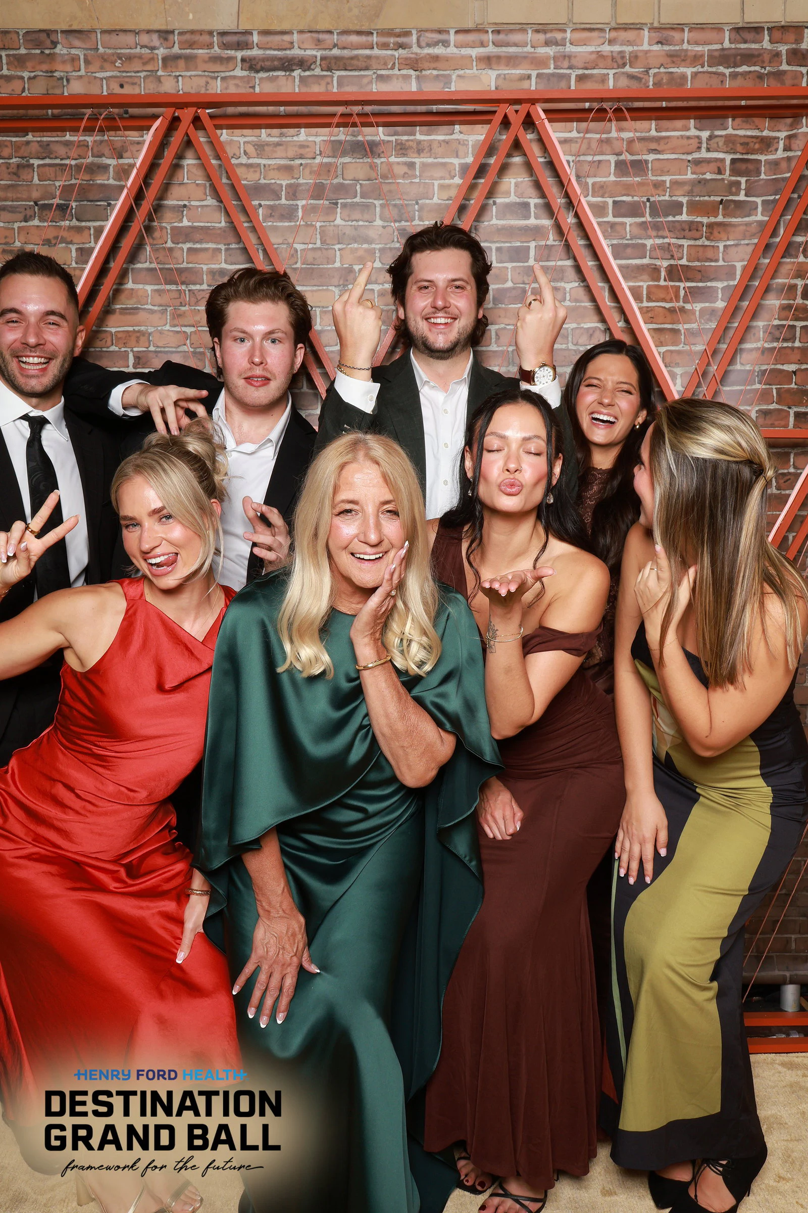 Ten guests in black tie and jewel-toned gowns packed in front of the brick wall at Henry Ford Health Grand Ball