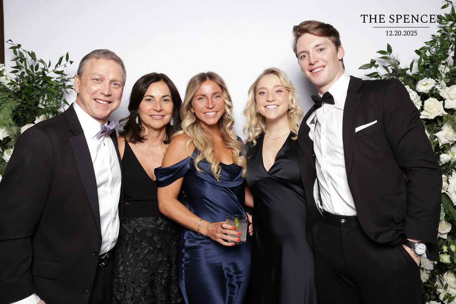 Two men in tuxedos with three women between them, one in a navy satin dress holding a drink at Jessica + Rory