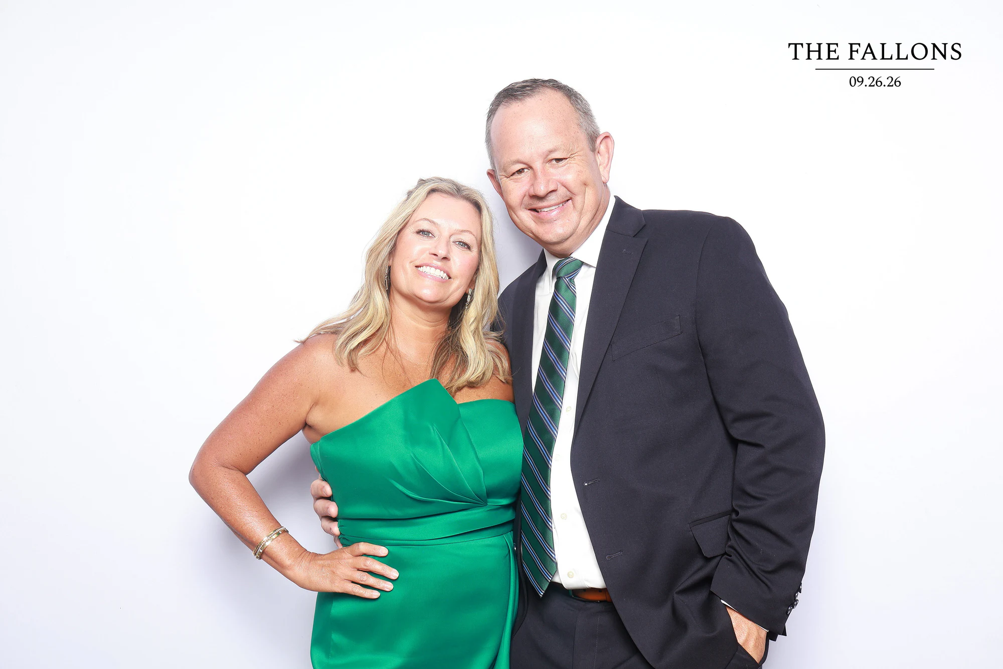 A woman in an emerald green dress and a man in a dark suit and striped tie smiling at the camera at Julia + Adam