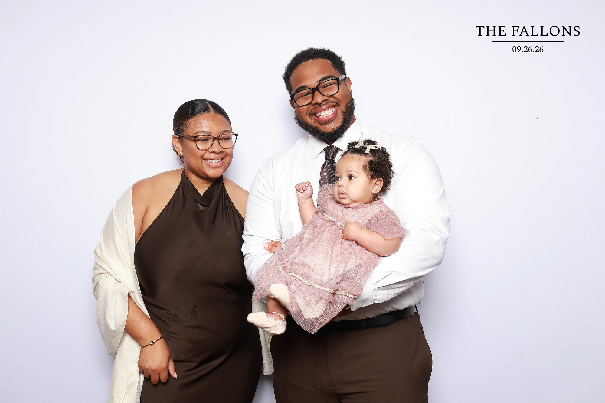 A couple holding their baby in a pink dress, both parents smiling at Julia + Adam