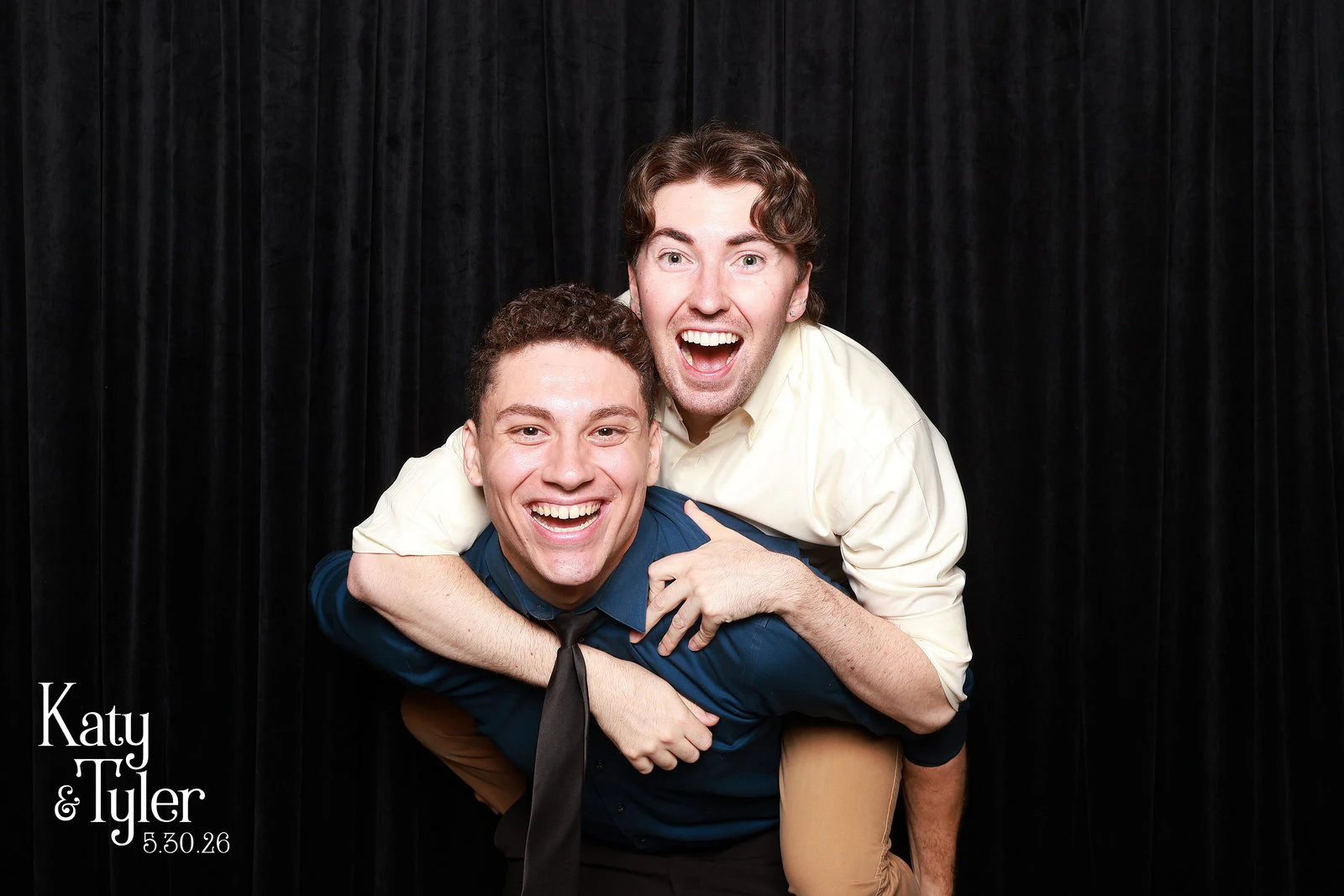 One man riding piggyback on another, both laughing at the camera at Katy + Tyler