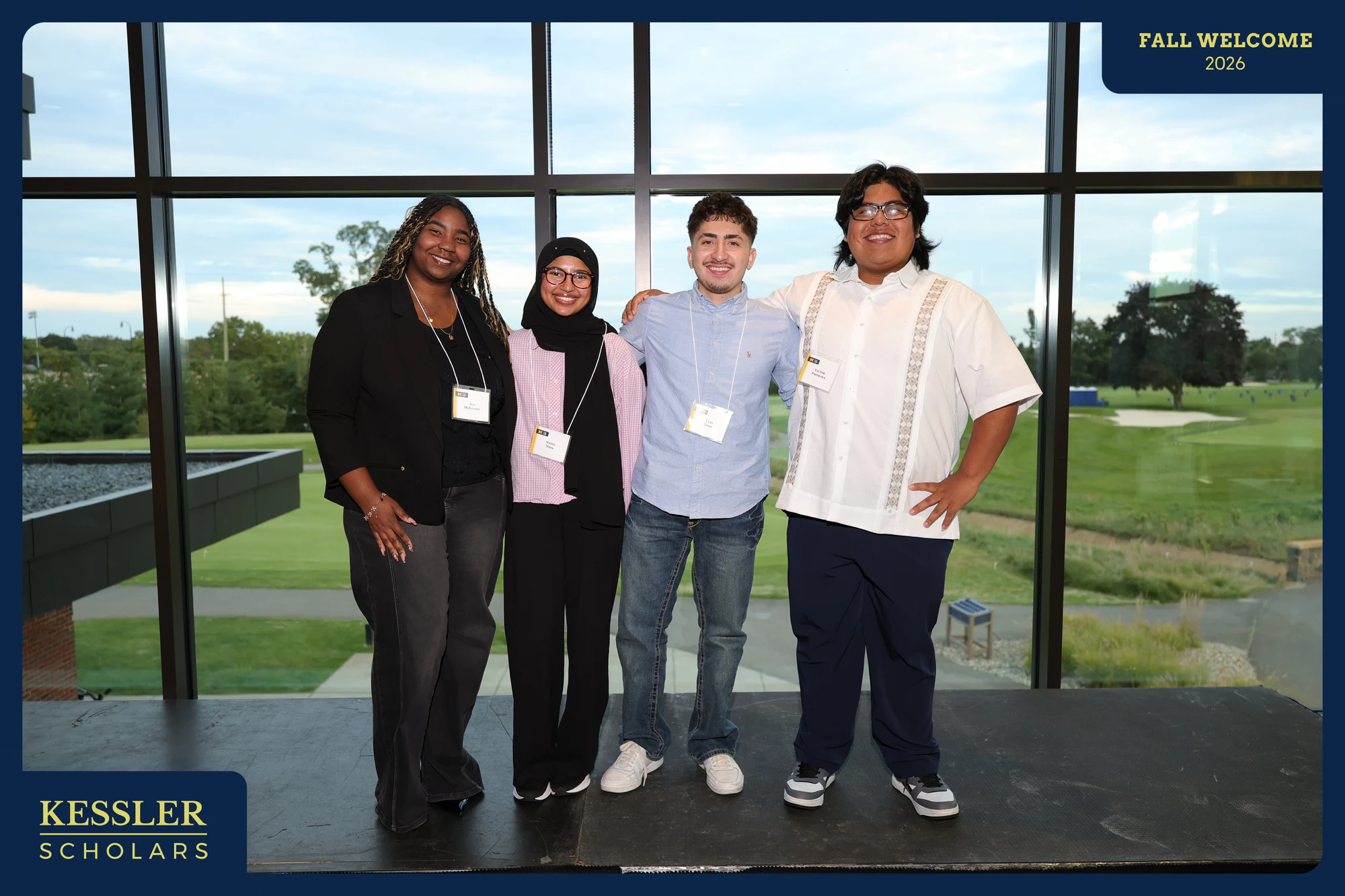 The same four students at the windows, standing a little farther apart at Kessler Fall Welcome Dinner