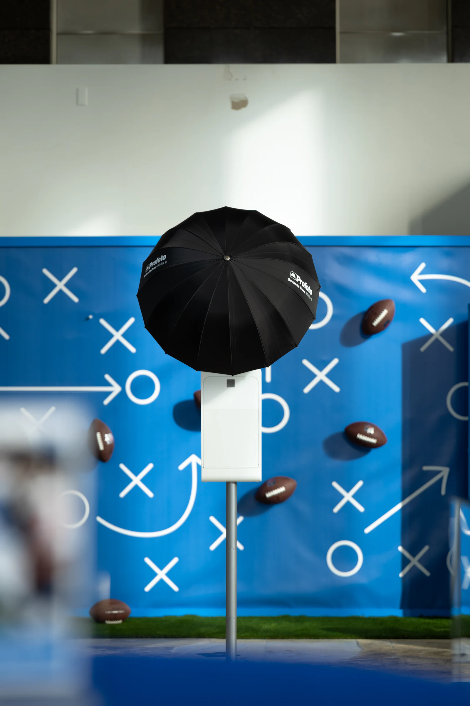 The booth and its black umbrella head-on against the blue playbook wall, footballs floating across the X's and arrows