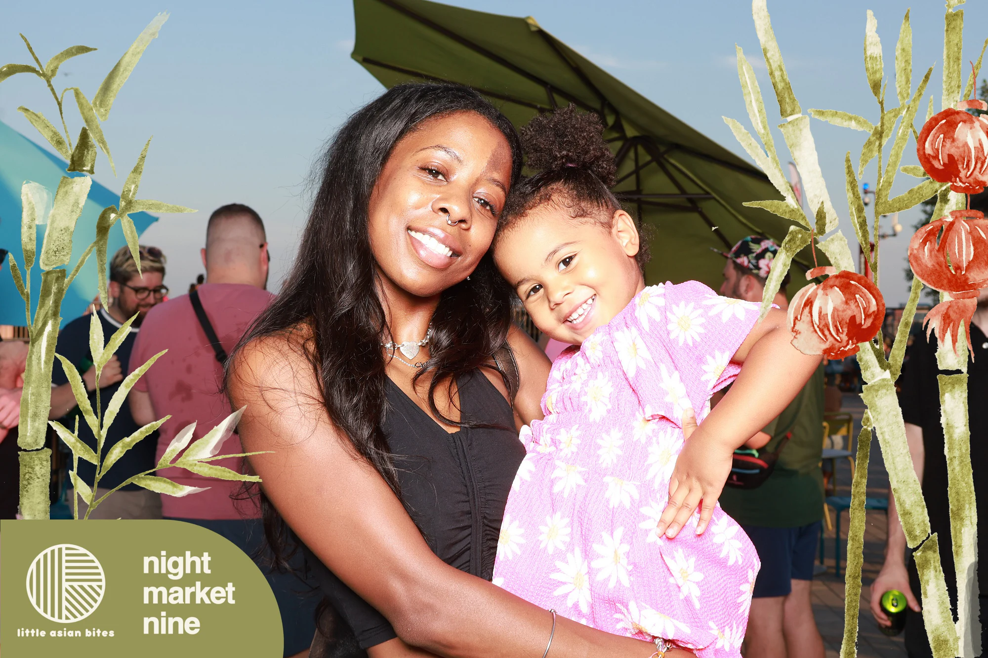 Mother holding her daughter, both smiling, golden hour on the riverfront at Little Asian Bites Night Market