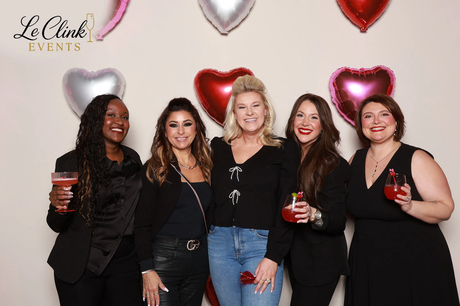 Five women in black, three holding red drinks, in front of heart balloons at LivCo Galentine’s