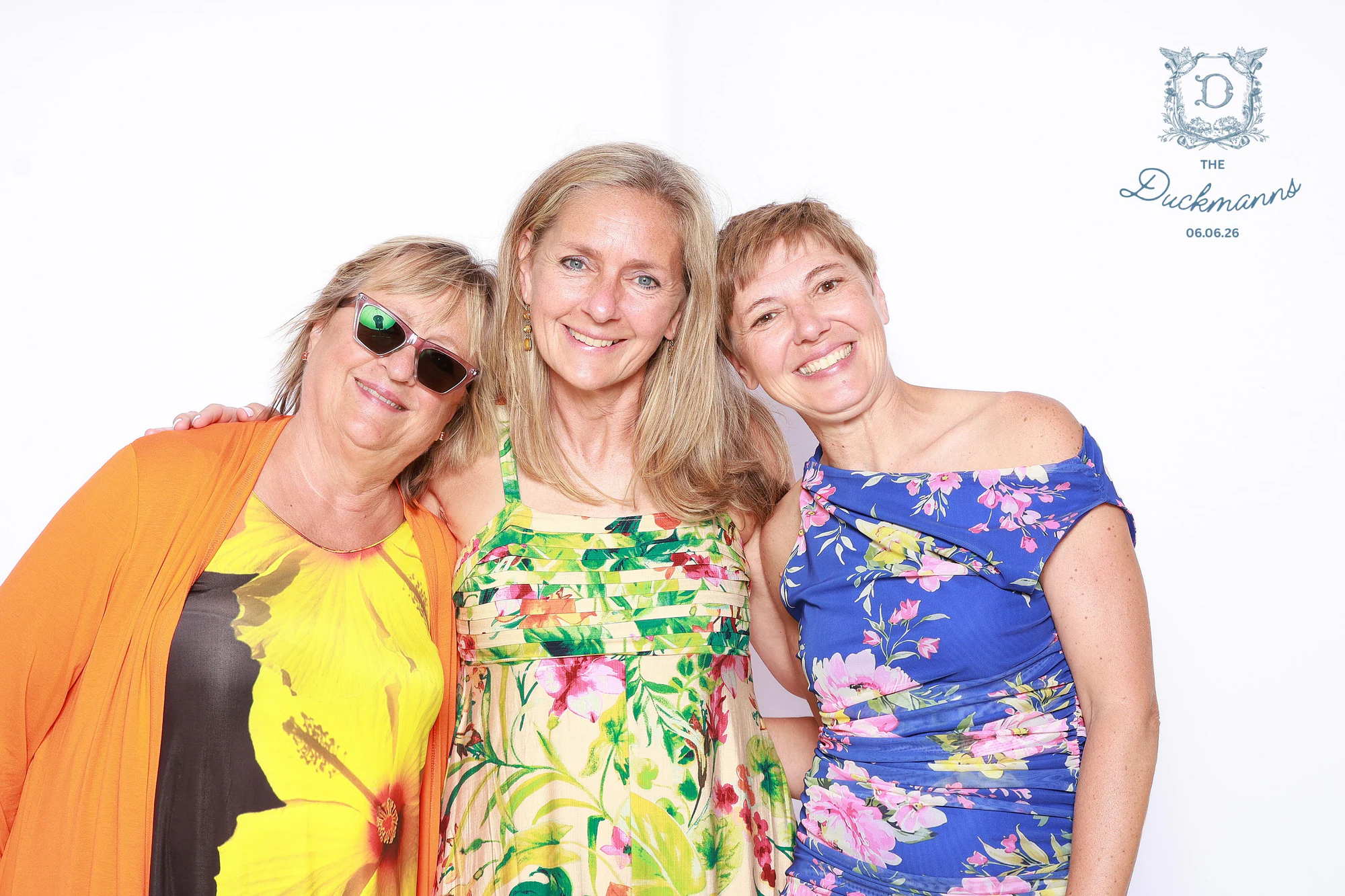 Three women in bright floral dresses with their heads together, one in green sunglasses at Melissa + Crosley