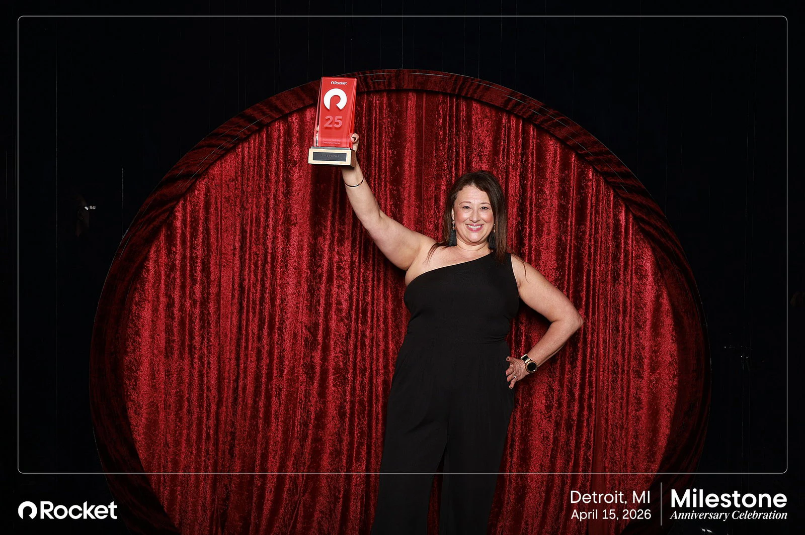 A woman in a black jumpsuit holding her plaque up over her head at Milestone Anniversary Celebration