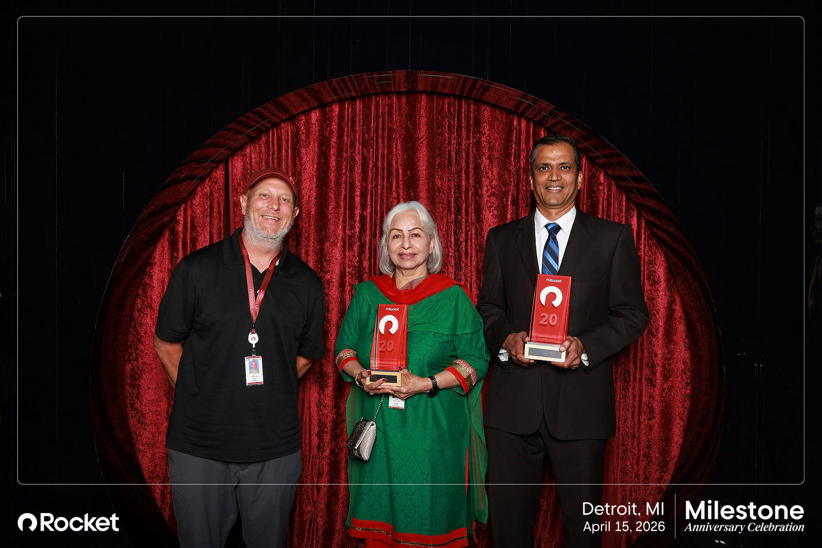 Two men and a woman in a green and red dress, two of them holding plaques at Milestone Anniversary Celebration