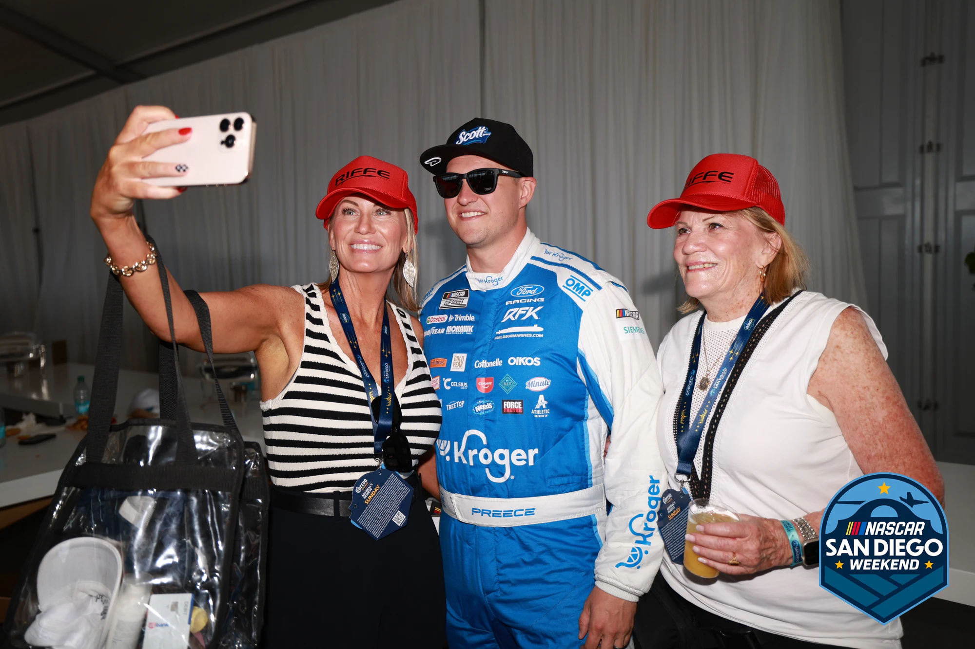 A driver in his firesuit stops for two fans, one of them shooting a selfie at NASCAR San Diego