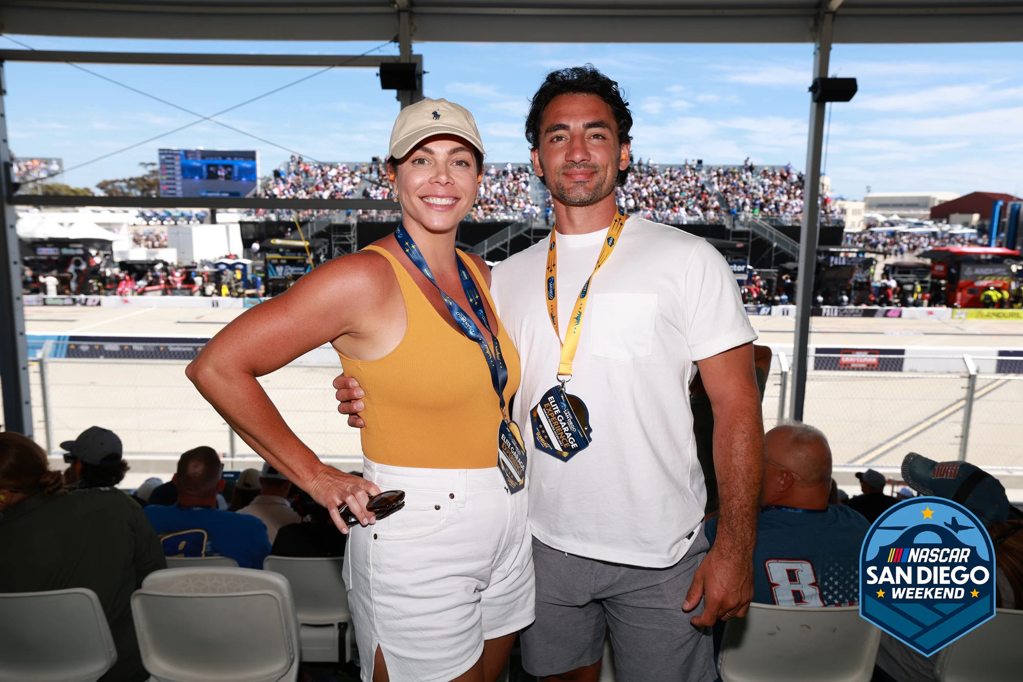 A couple posed together on the deck, the packed grandstand behind them, at NASCAR San Diego