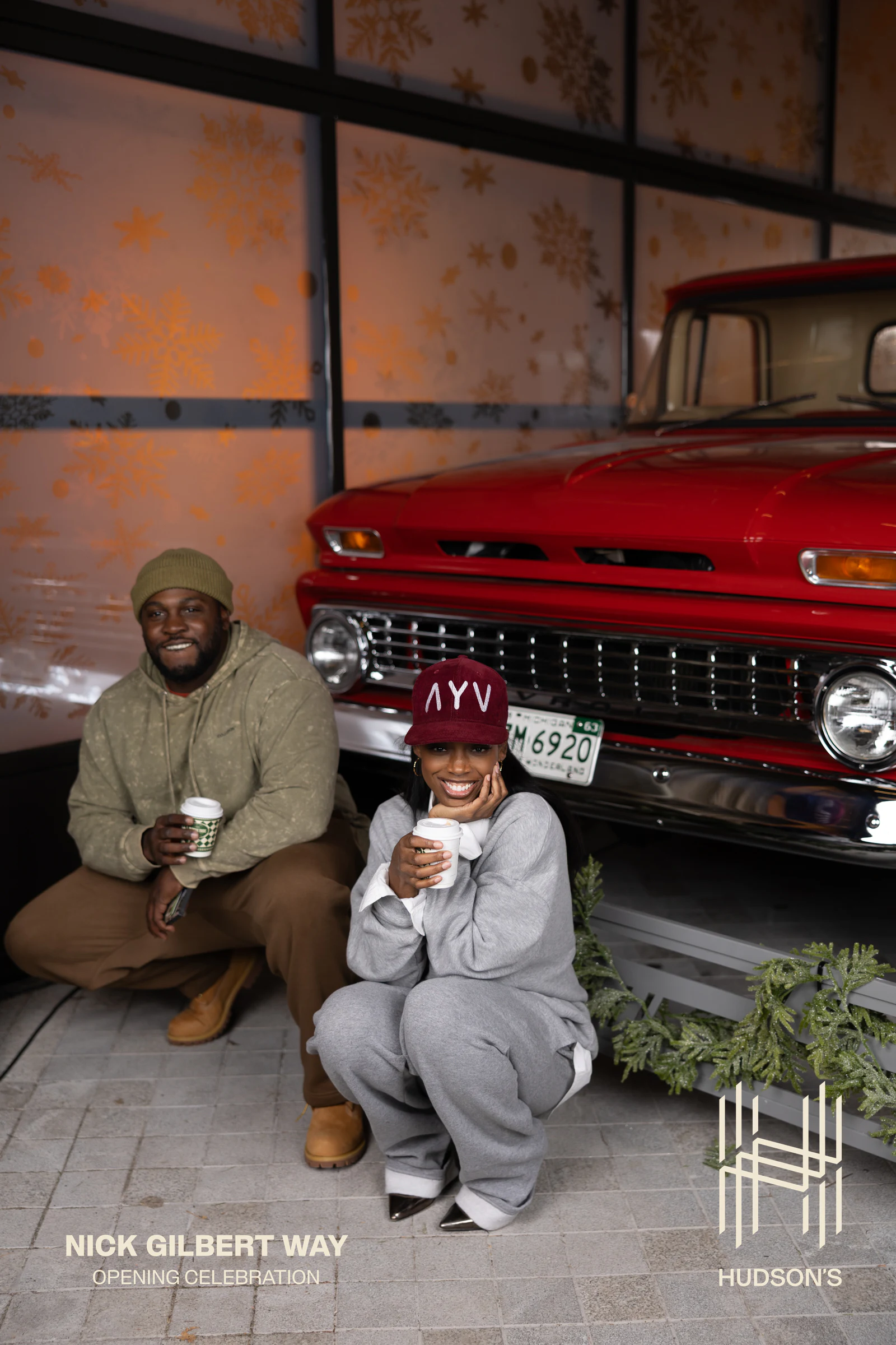Couple crouched by the grille with their drinks, laughing at each other at Nick Gilbert Way Opening Celebration