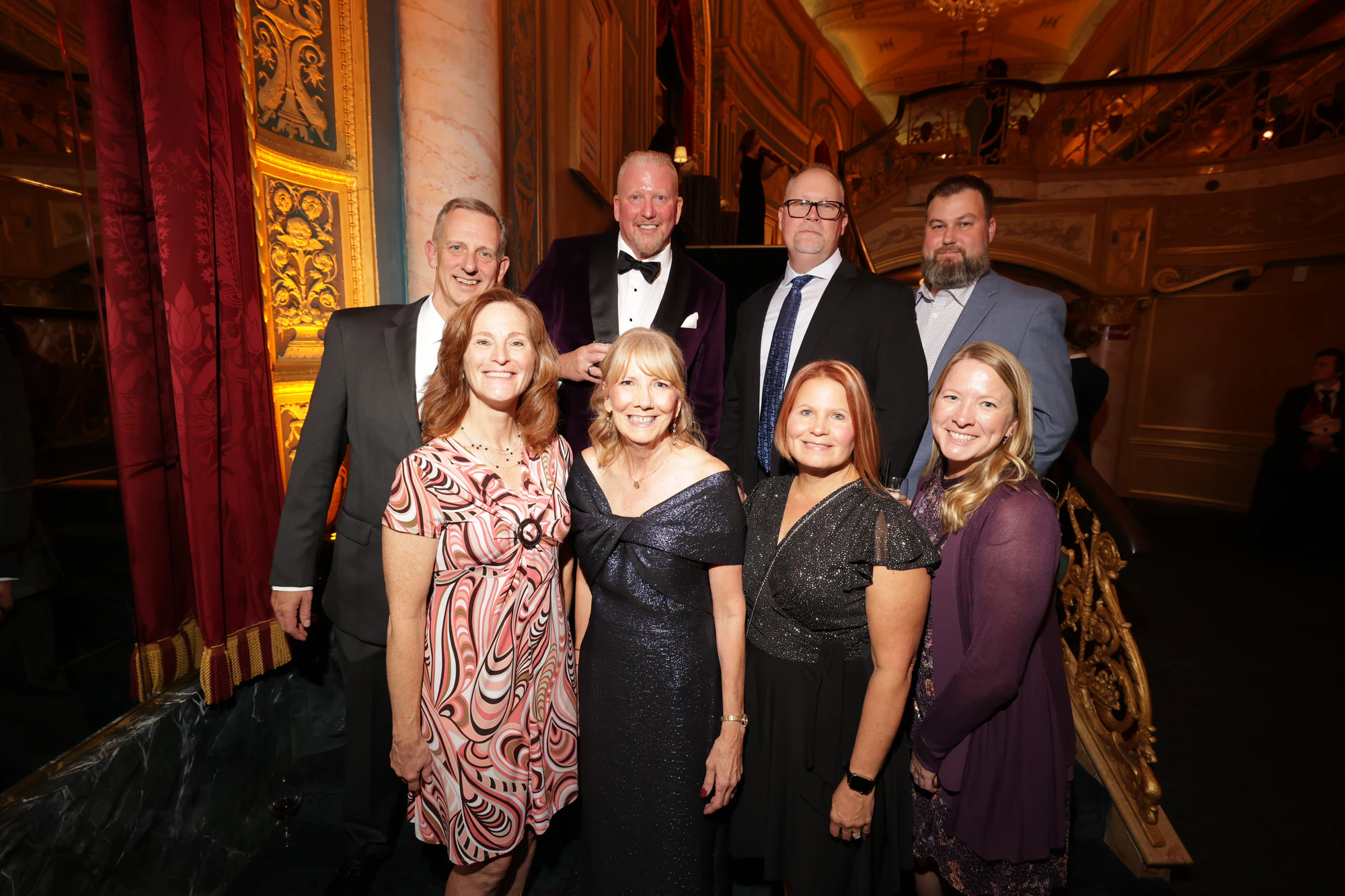 Nine guests in suits and evening dresses, four standing behind five at the surprise engagement party at the Detroit Opera House