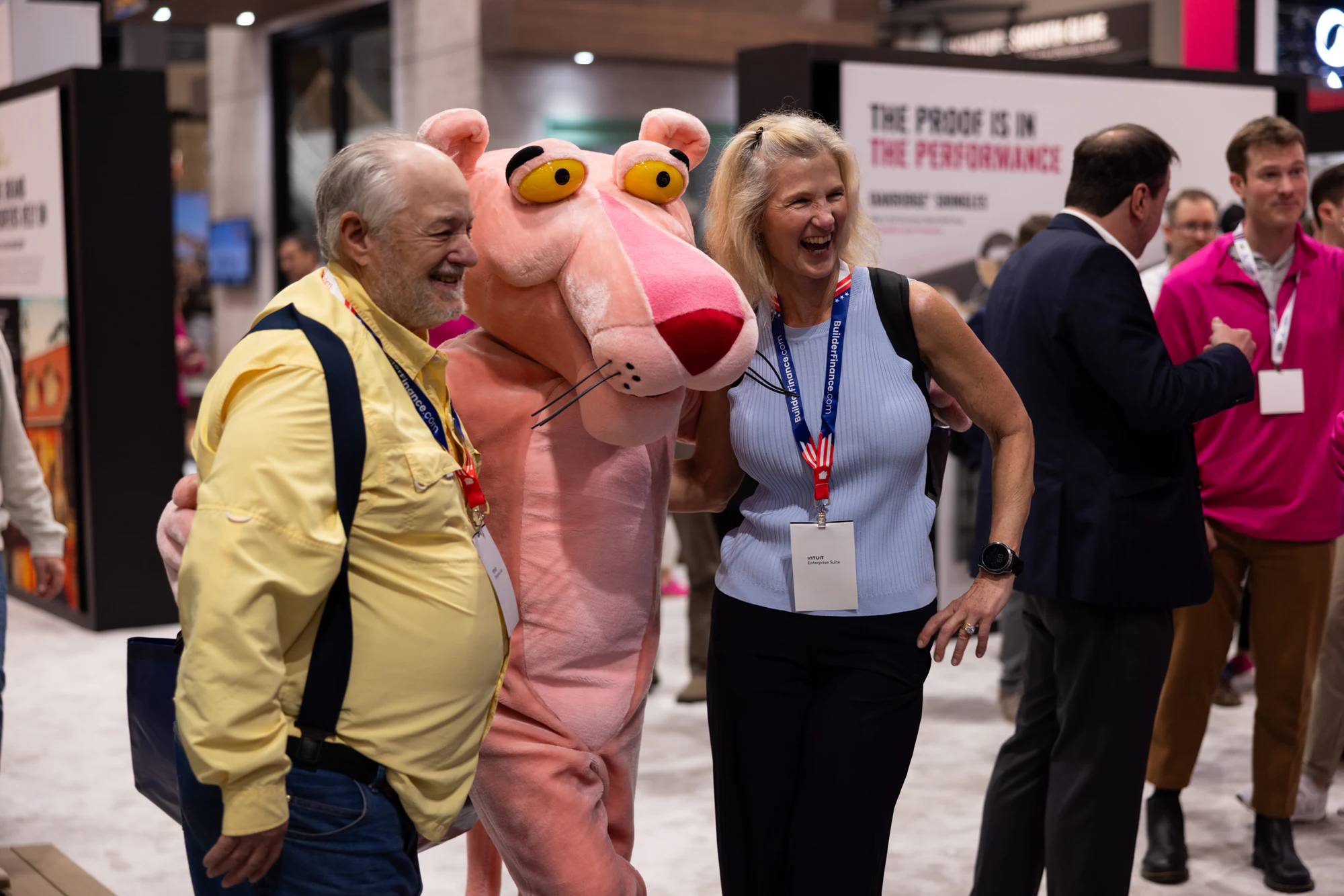 Panther squeezed between two attendees, both grinning at Owens Corning at IBS 2026