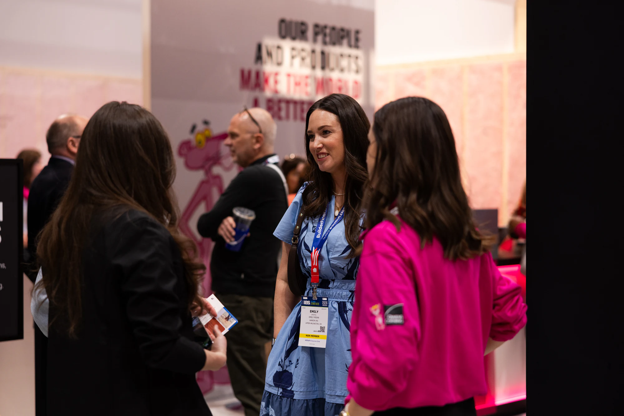 Pink-shirt rep mid-conversation with a guest, smiling at Owens Corning at IBS 2026
