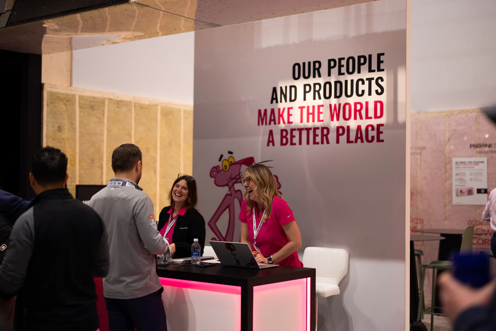 Two at the pink counter under the Panther mural at Owens Corning at IBS 2026