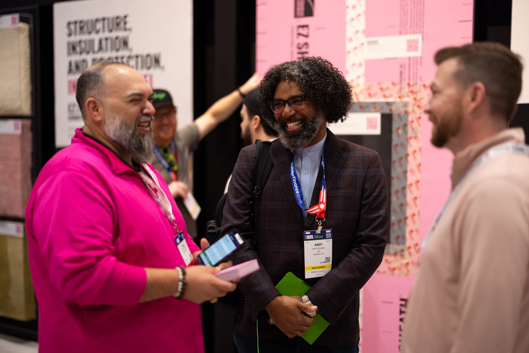 Two guests laughing against the pink insulation wall at Owens Corning at IBS 2026