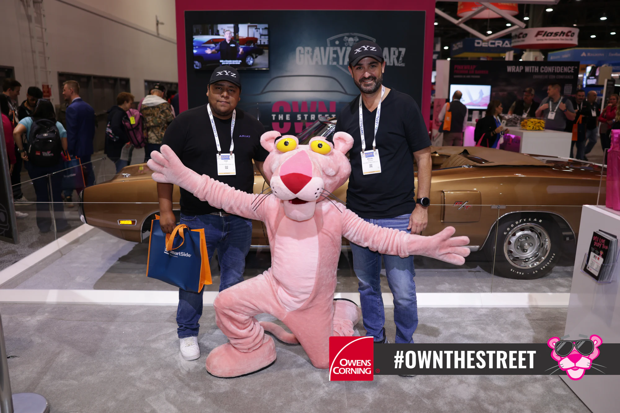 Pink Panther throwing its arms wide beside two guests at Owens Corning at IRE 2024