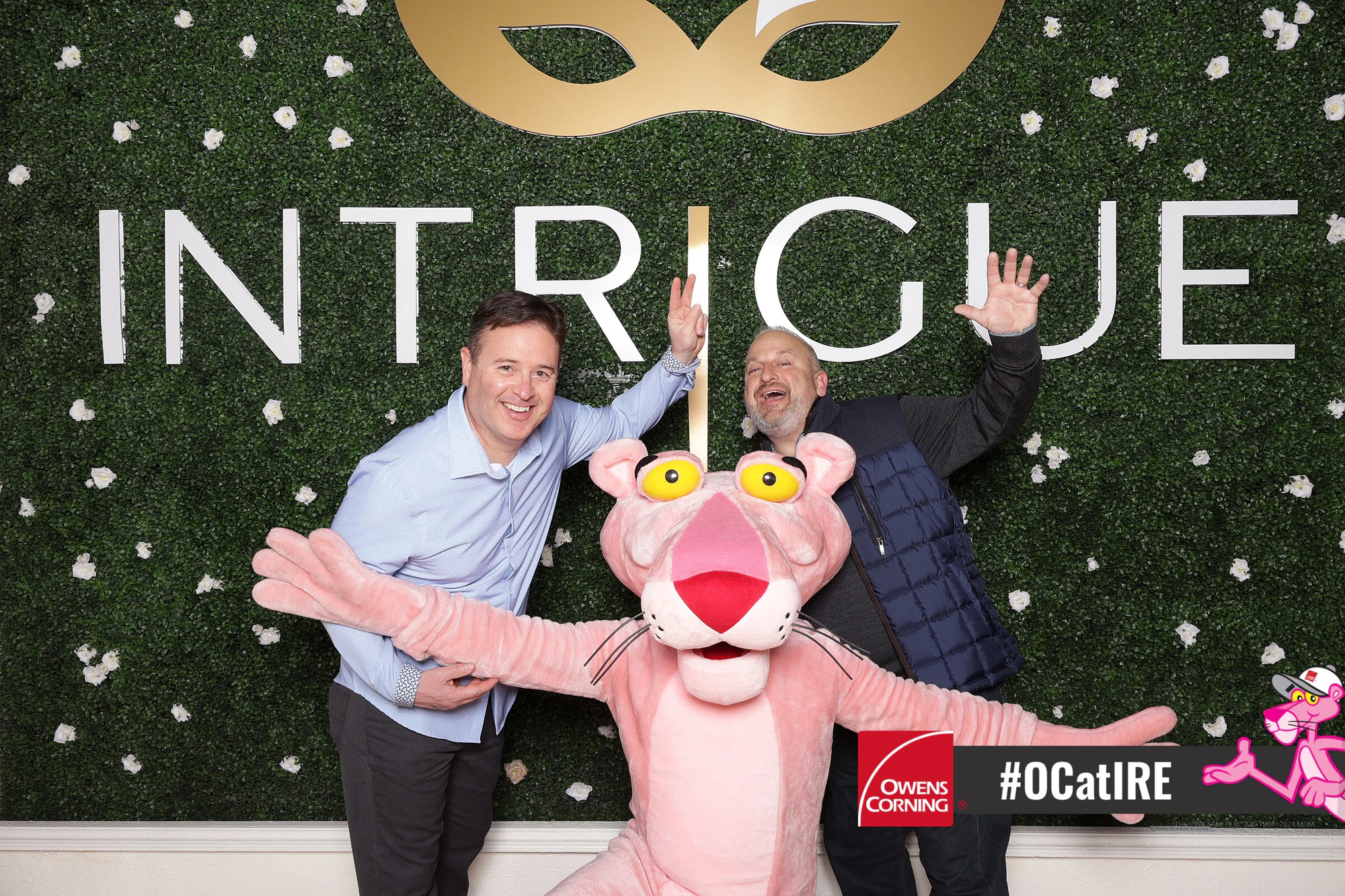 Guest and Pink Panther matching wide-arm poses under the Intrigue mask logo at Owens Corning at IRE 2024